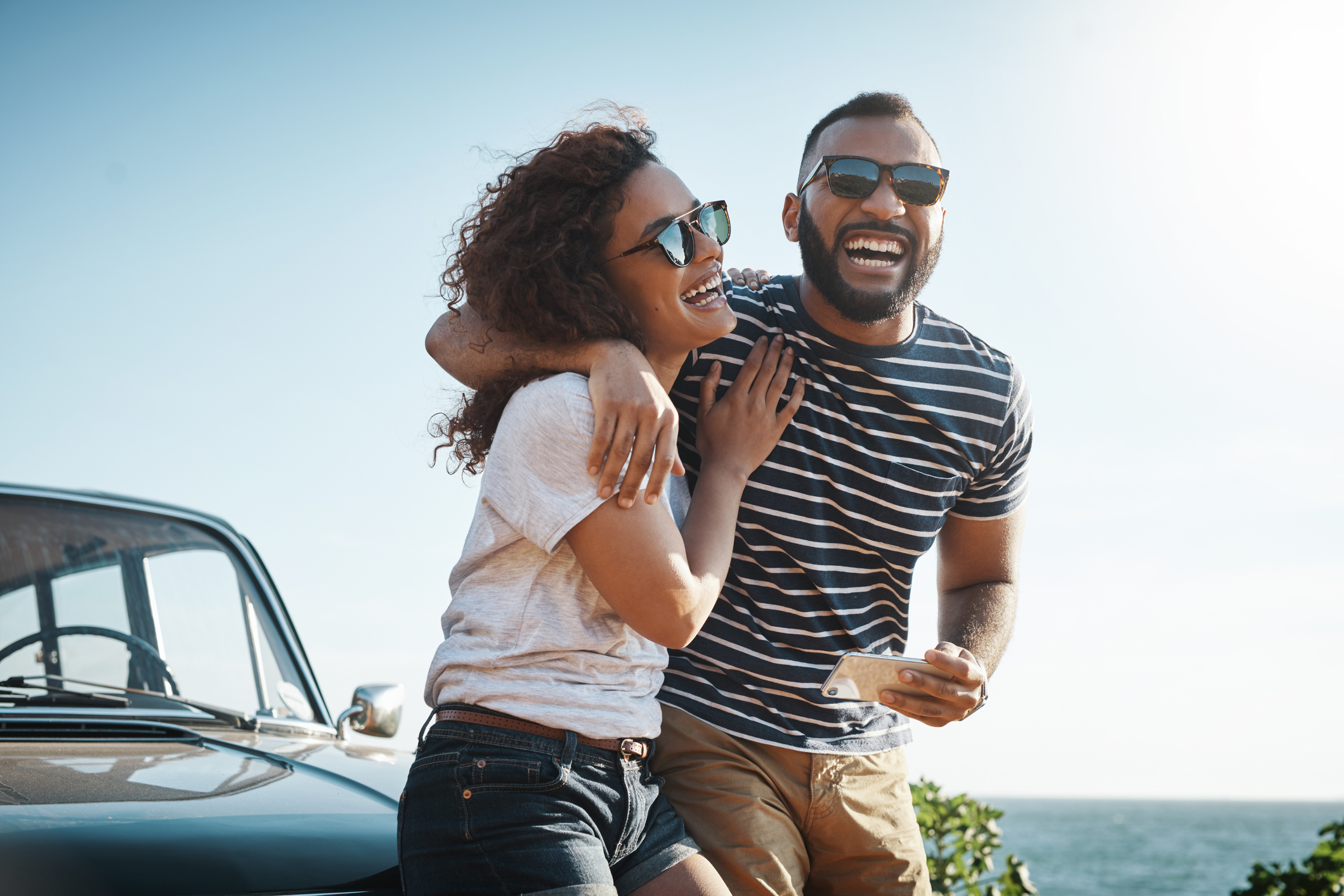 Man and woman laughing together beside a car on a sunny day, representing joyful parenting moments