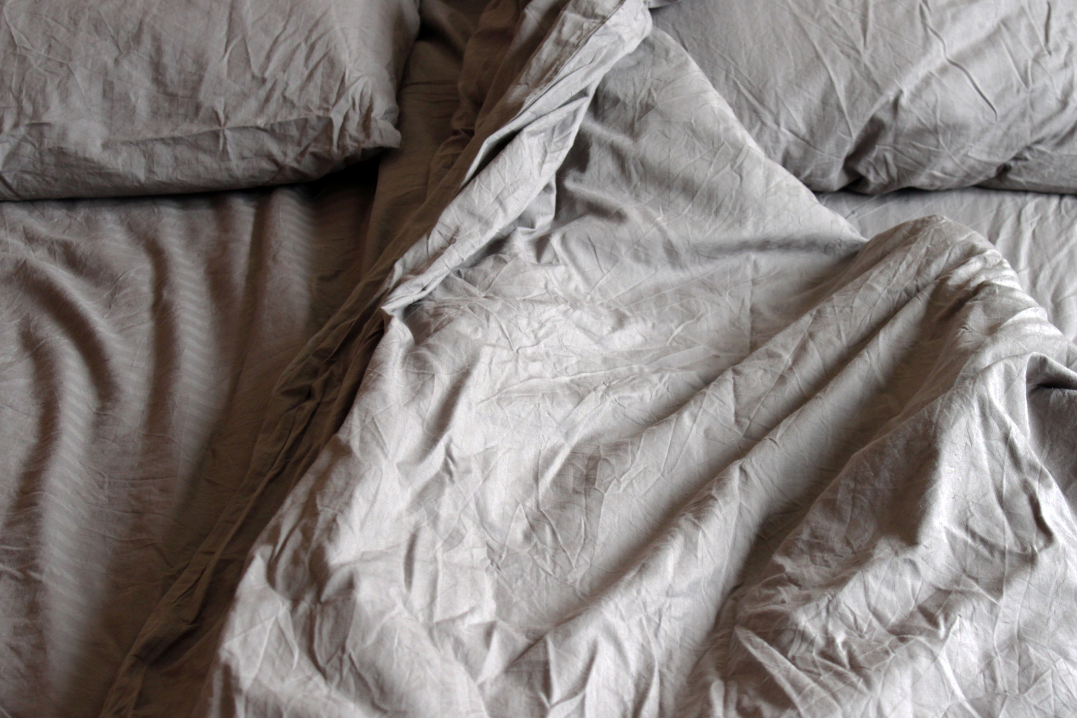 Unmade bed with crumpled sheets and pillows, suggestive of recent use