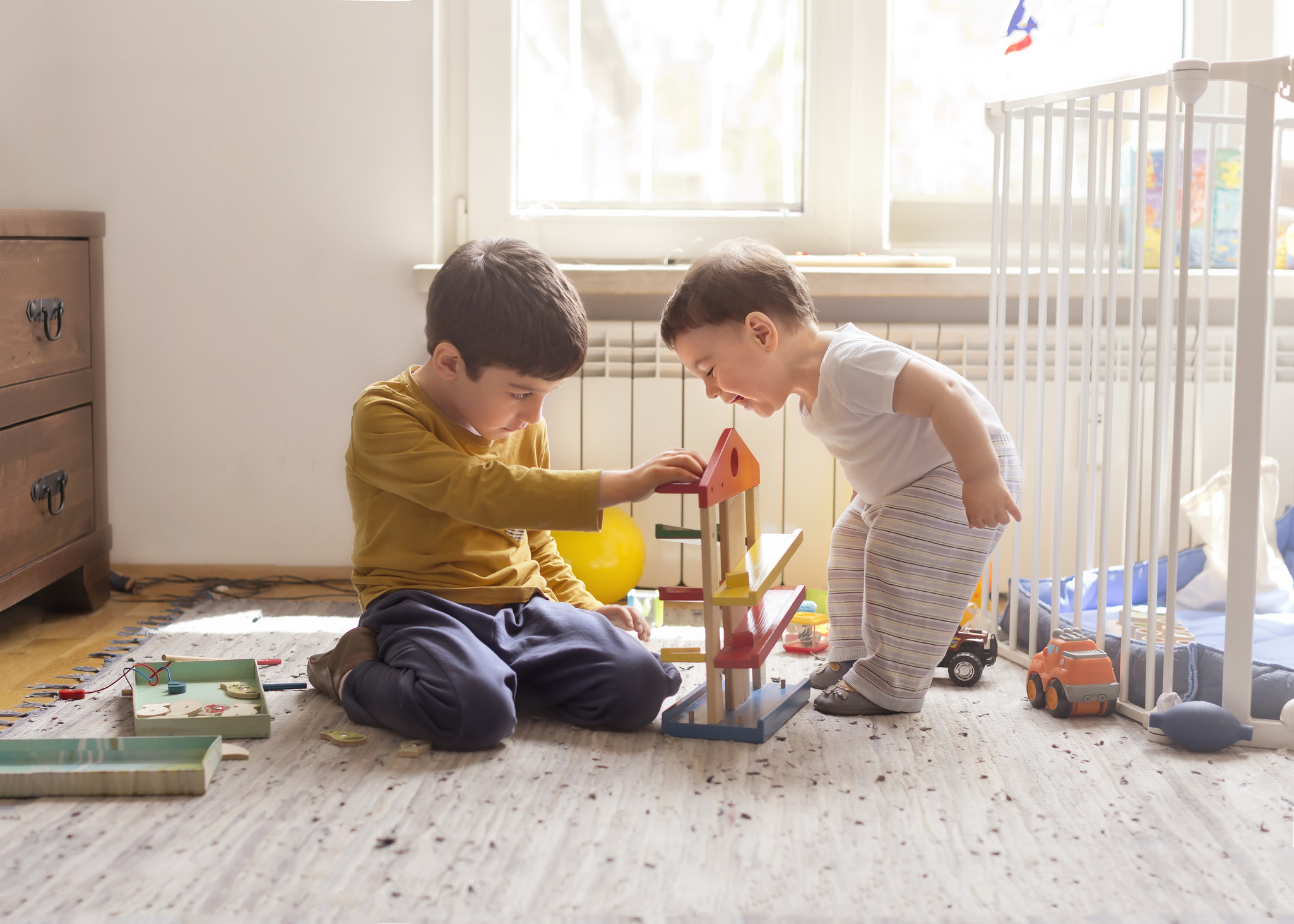 Two children playing with toys on a sunny room floor