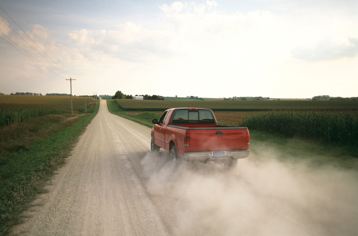A pickup truck driving away on a dusty rural road
