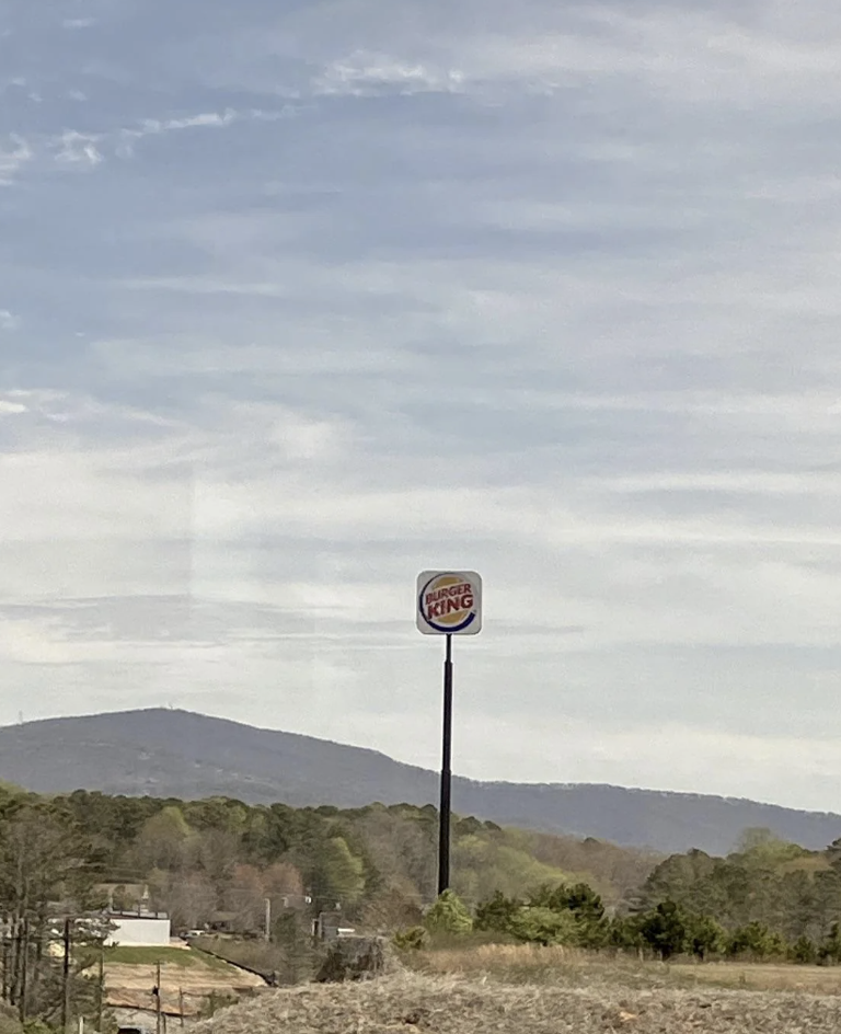Tall sign with Burger King logo against a landscape with trees and a hill