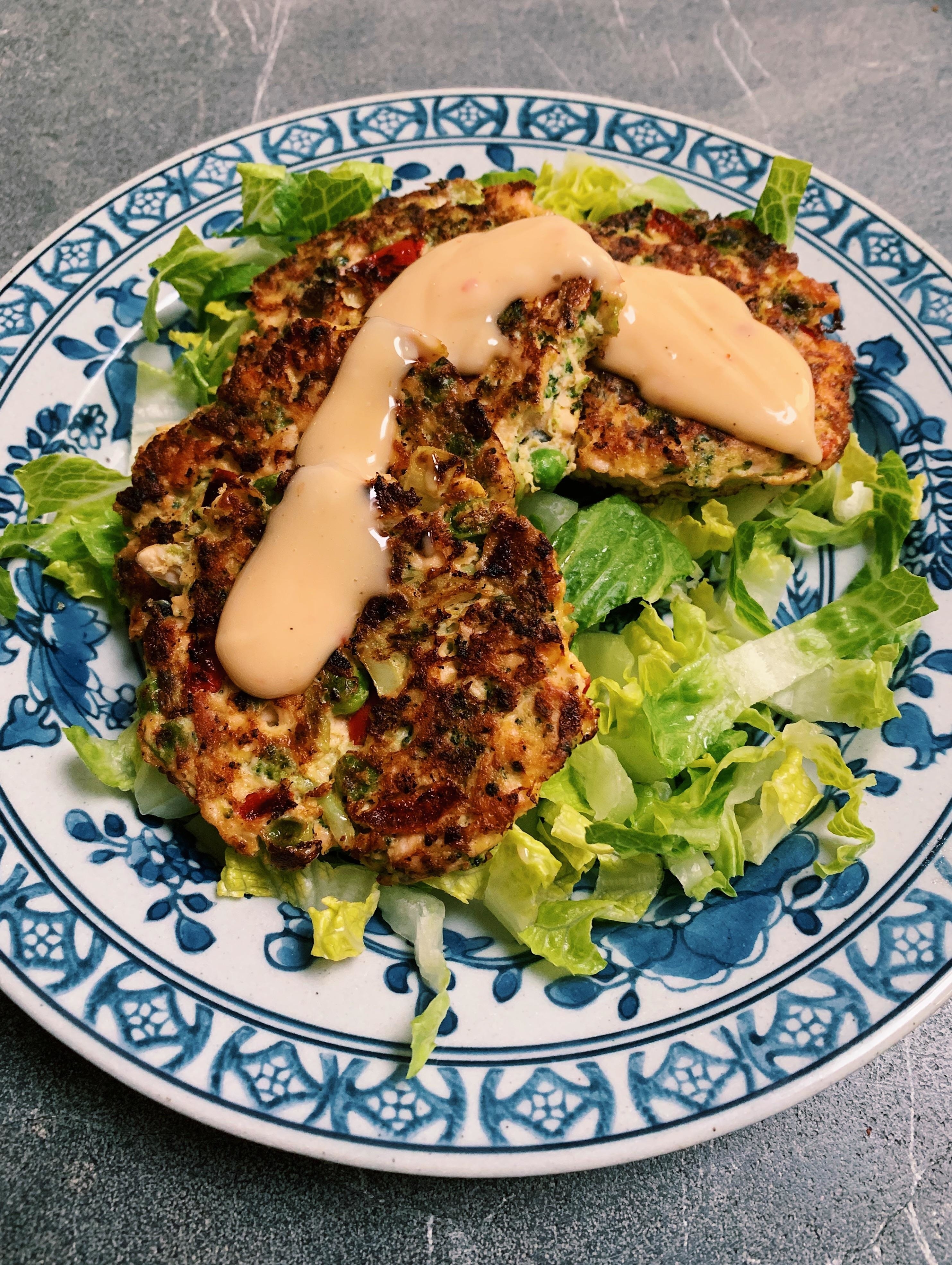 Two chicken patties over lettuce on a blue patterned plate, with drizzled sauce