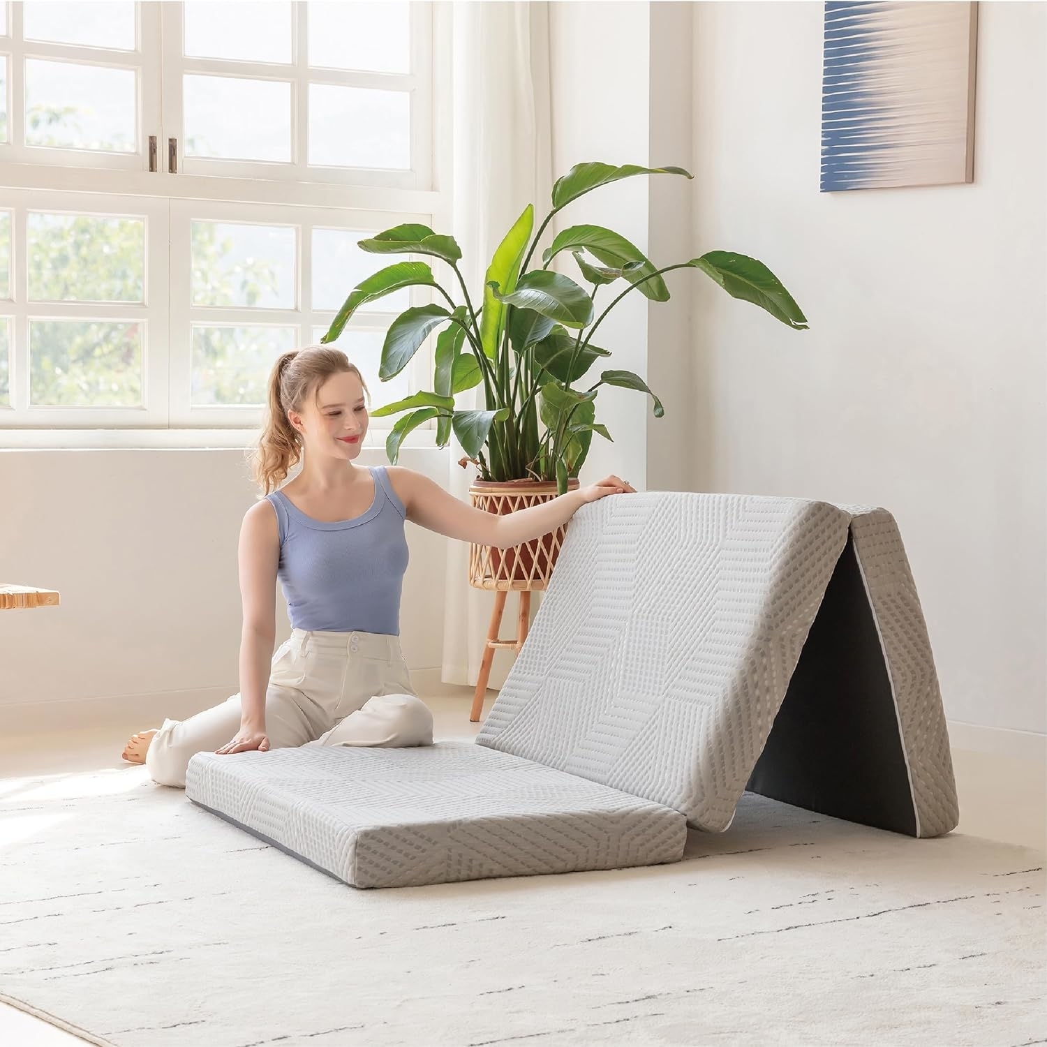 Woman sitting next to an open, foldable mattress, suitable for compact living spaces