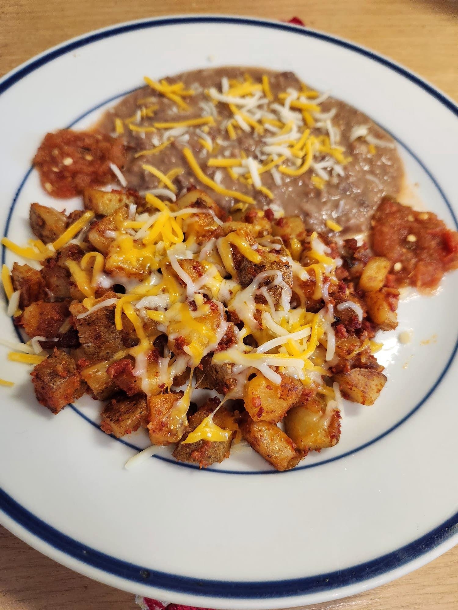 A plate of breakfast with hash browns, cheese, and beans