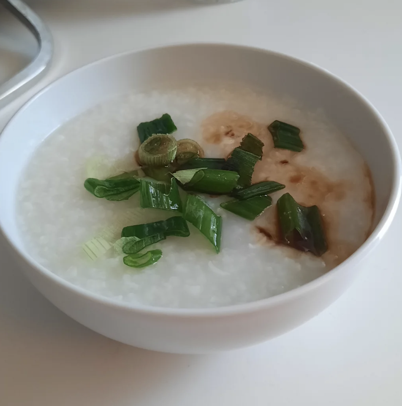 Bowl of rice porridge topped with green onions and a brown sauce