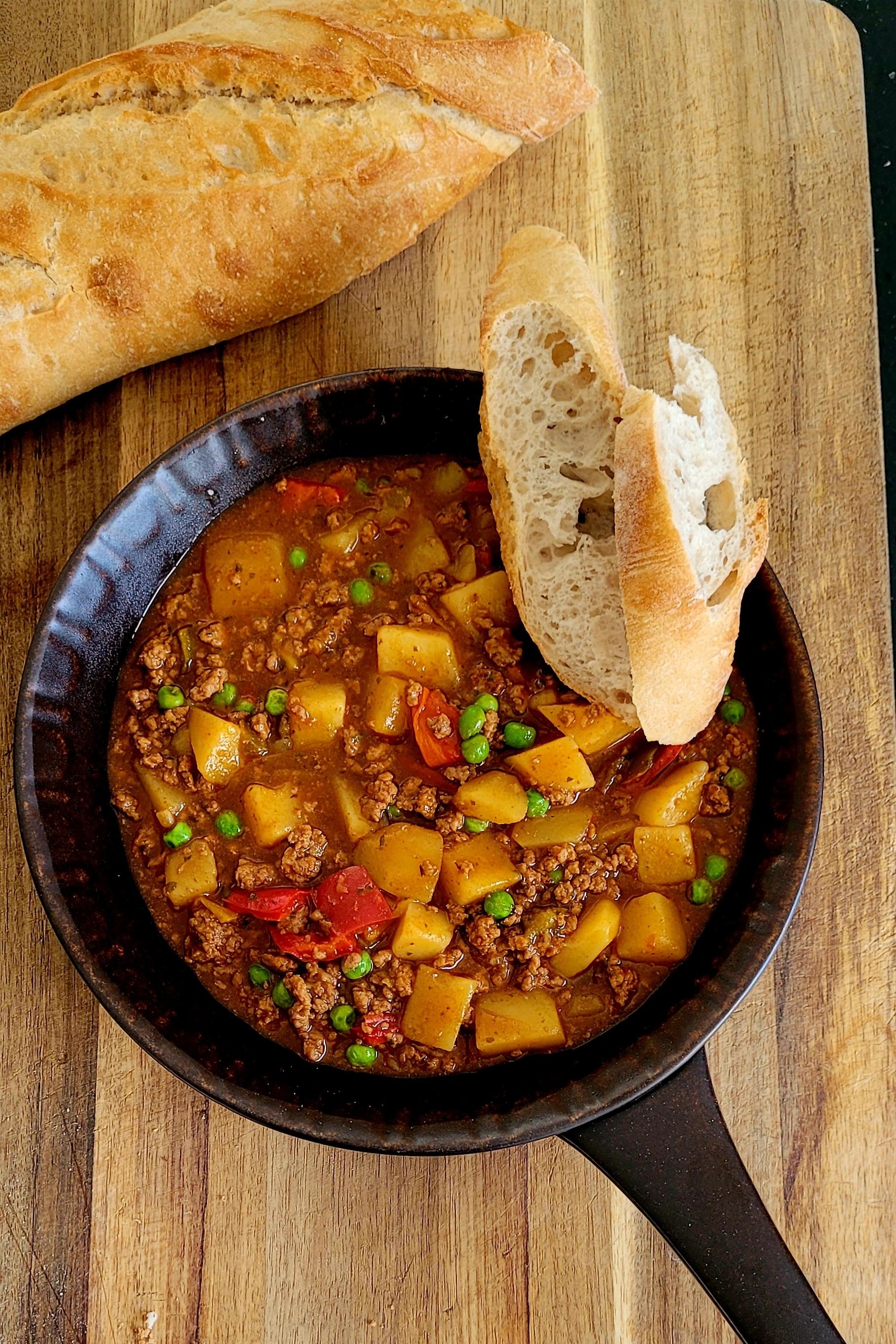 Ground beef and vegetable stew in a skillet, served with a side of bread
