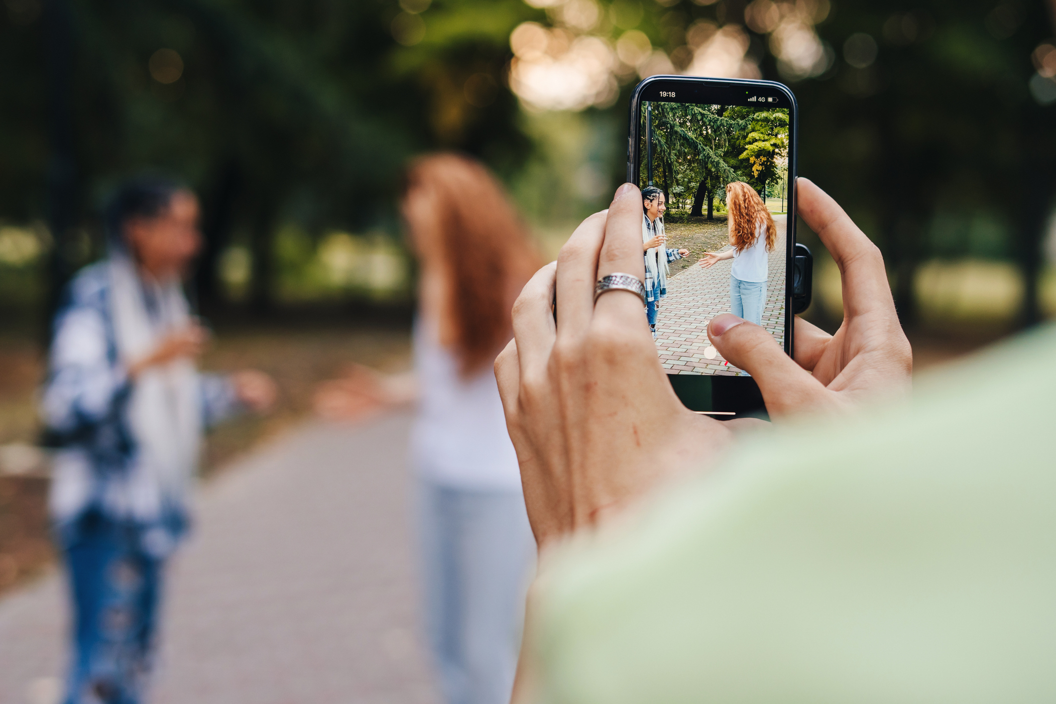 Person takes photo of two others walking in a park on a smartphone