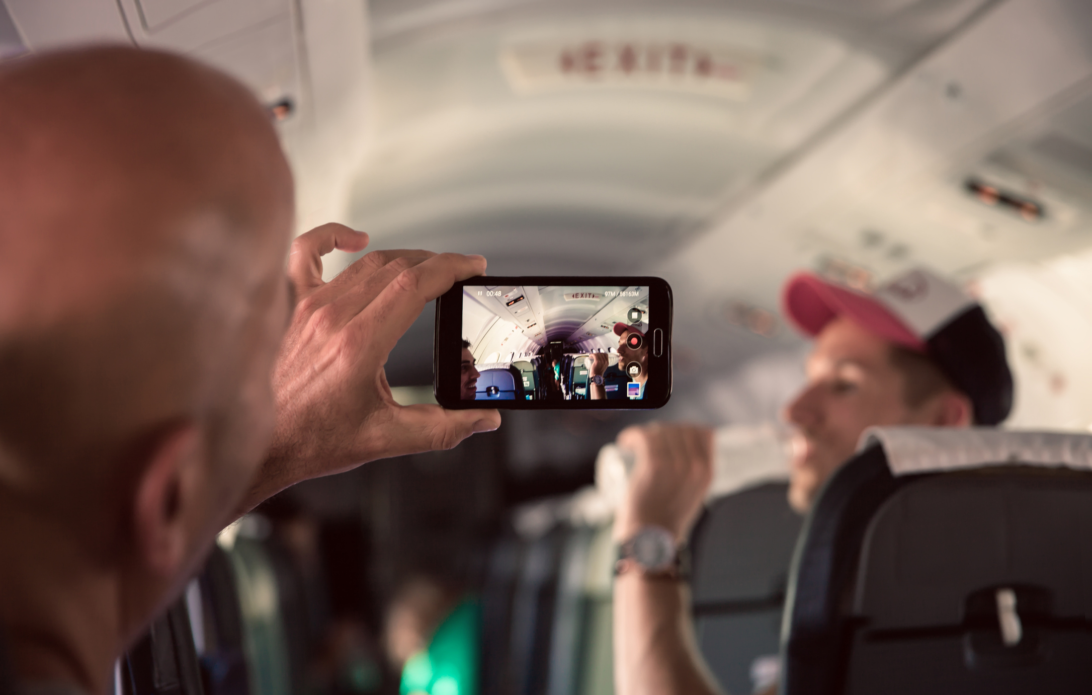 Person taking photo inside airplane with smartphone capturing other passengers