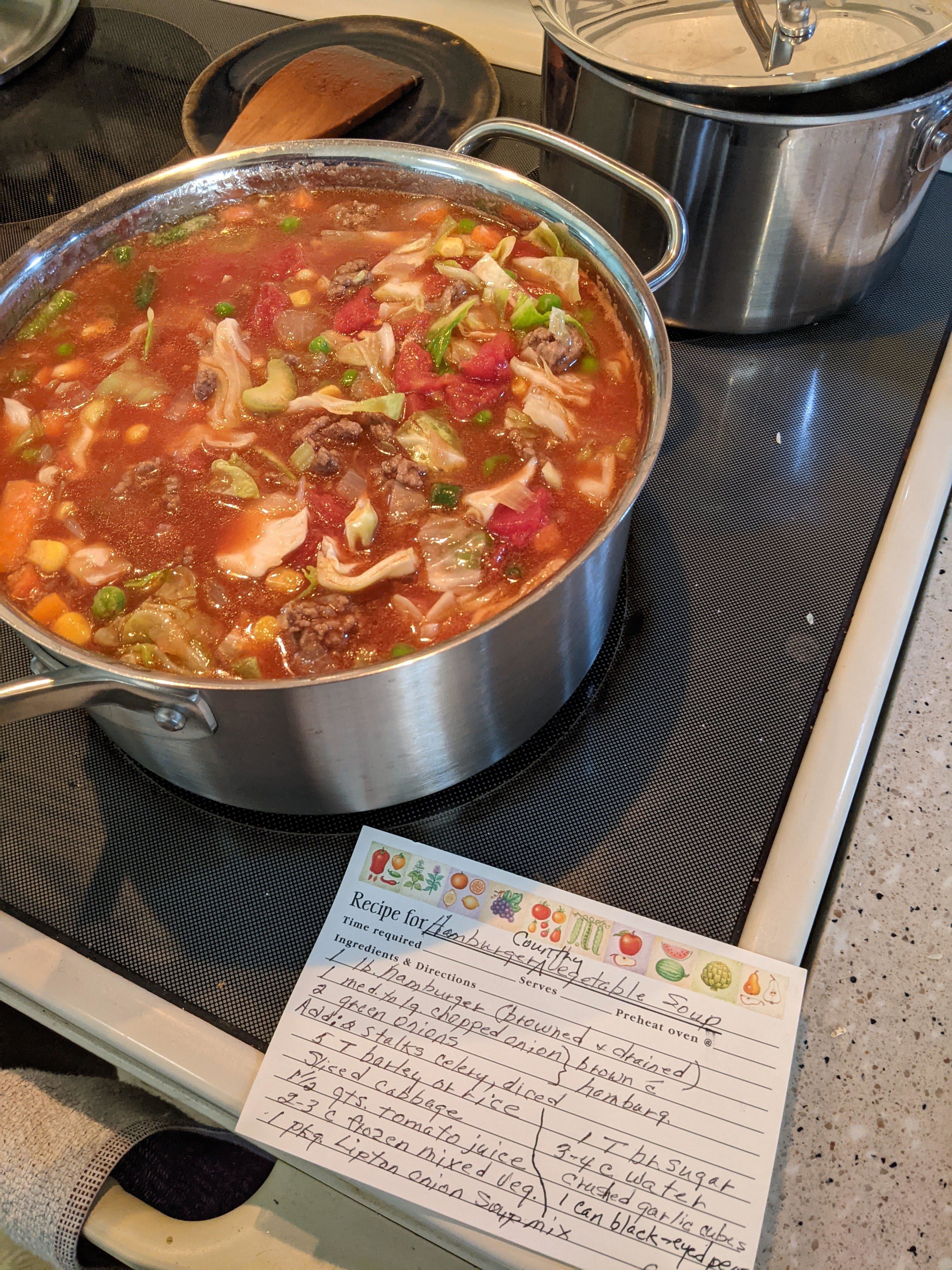 A pot of homemade soup on a stove with a handwritten recipe card in front