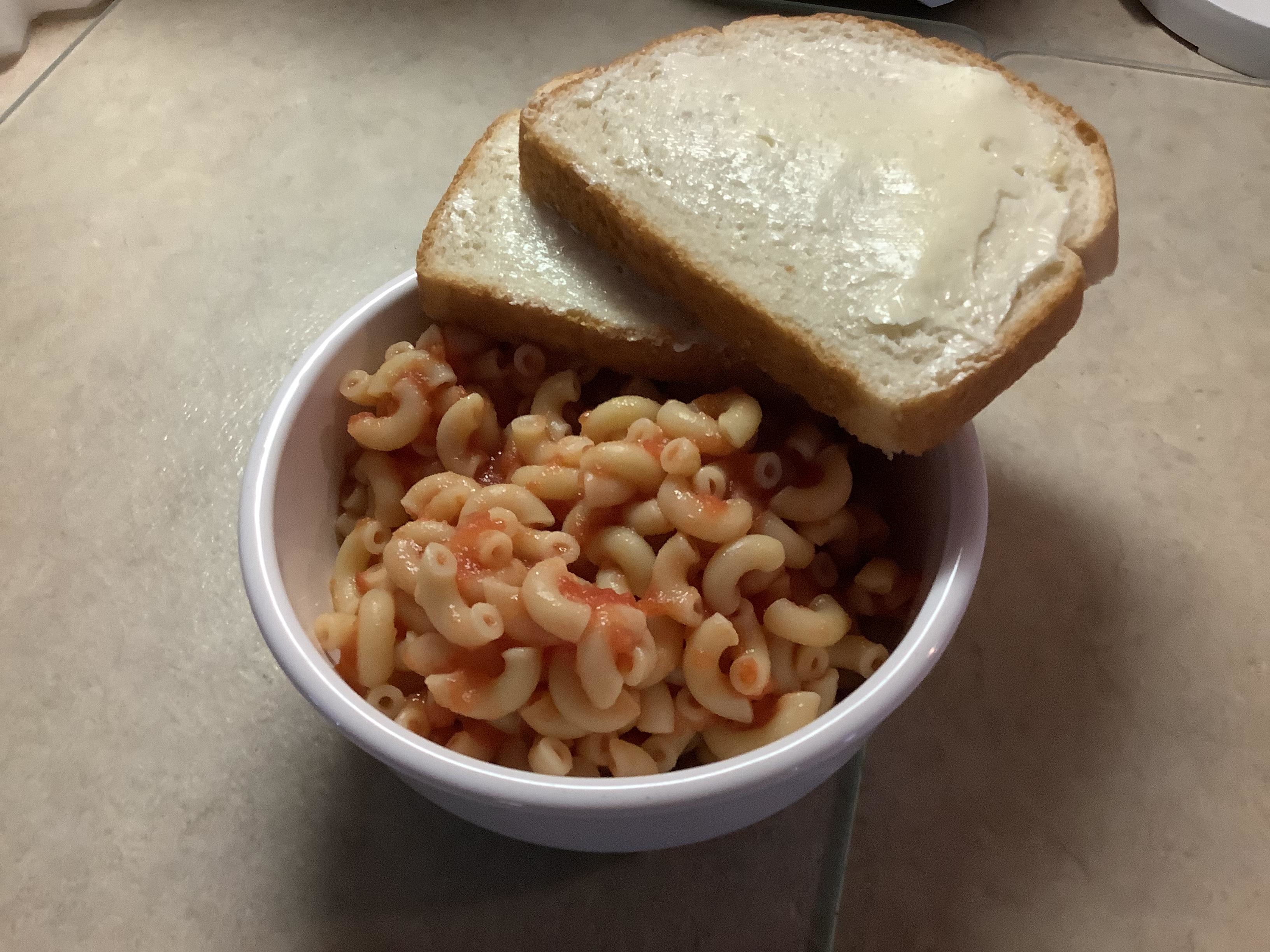 A bowl of pasta with a slice of buttered bread on top