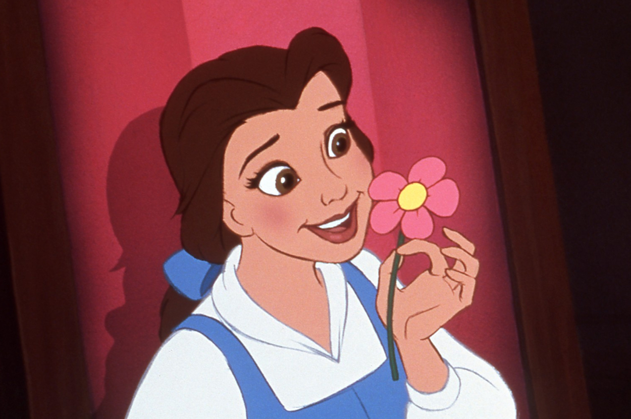 Belle from Beauty and the Beast holds a pink flower, smiling. She wears a white blouse under a blue dress