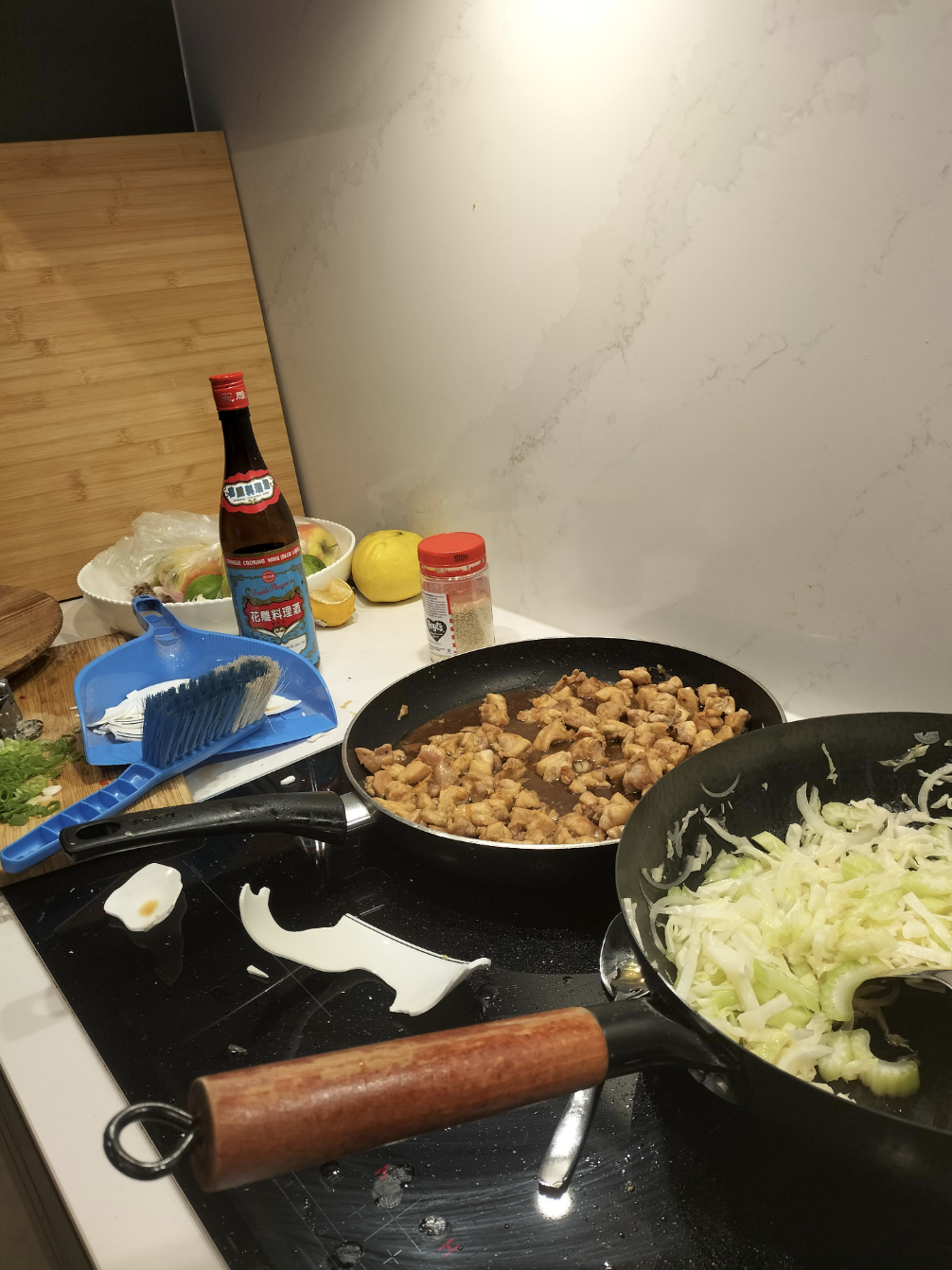 A kitchen counter with ingredients and cookware; a pan of cooked chicken and another with shredded cabbage