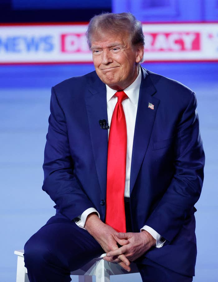 Trump in suit with tie sitting, smiling during an event