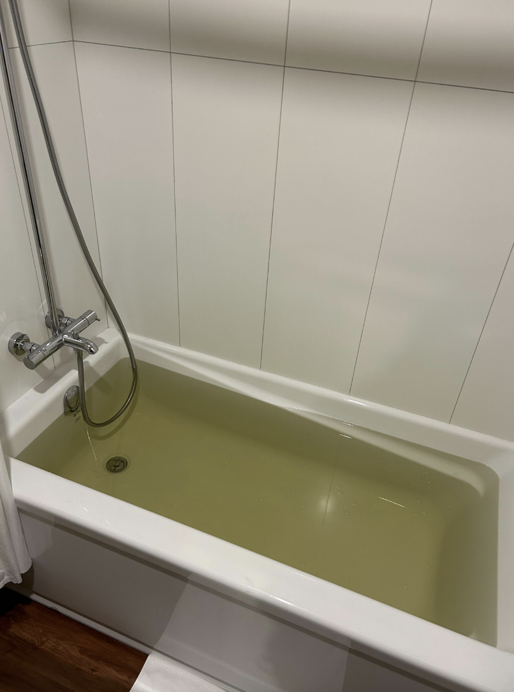 A bathtub filled with water, showing an attached showerhead to the right