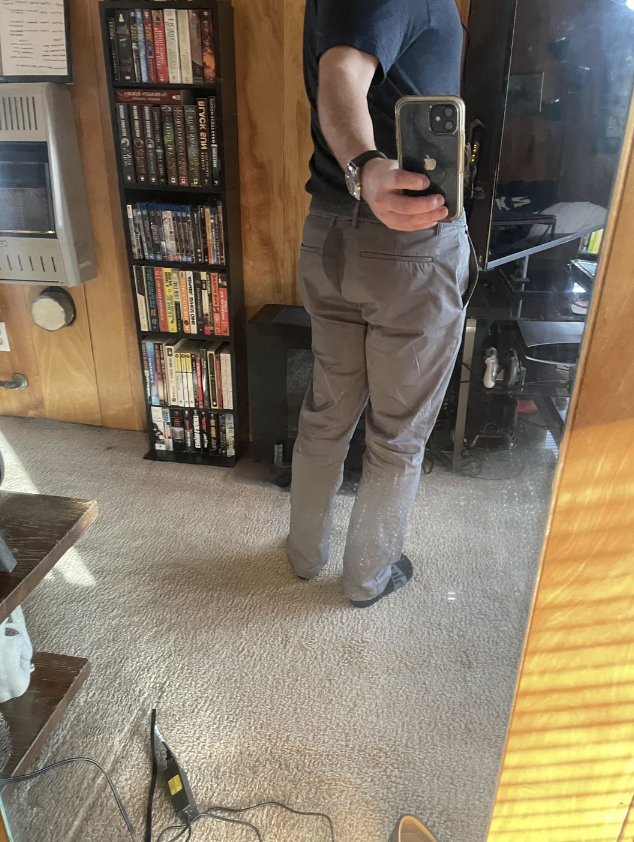 Person in a mirror selfie, wearing a t-shirt and cargo pants, smartphone in hand, indoors