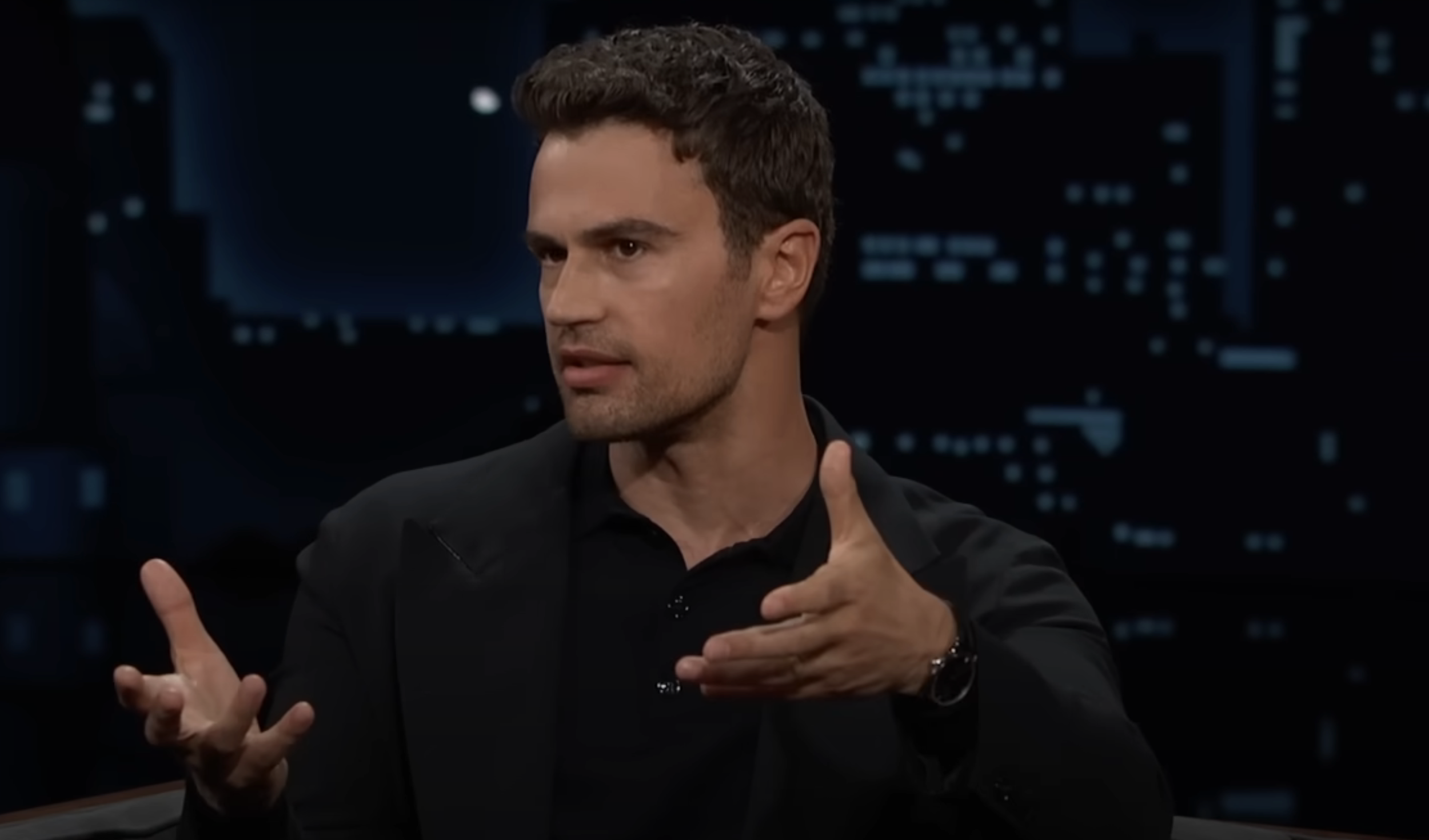 Man in black shirt gestures while speaking on a talk show