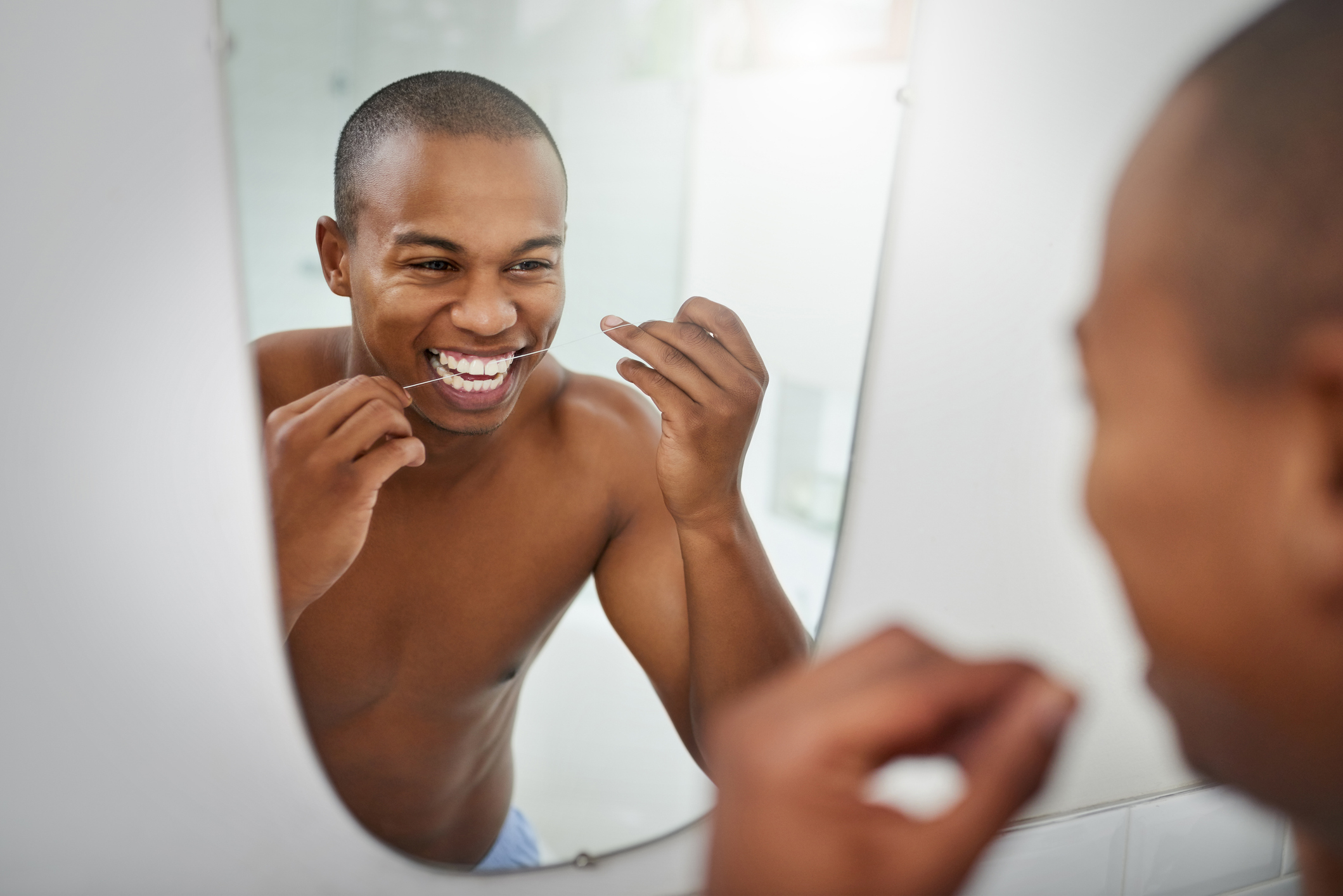 Person flossing teeth while smiling at mirror, promoting dental hygiene