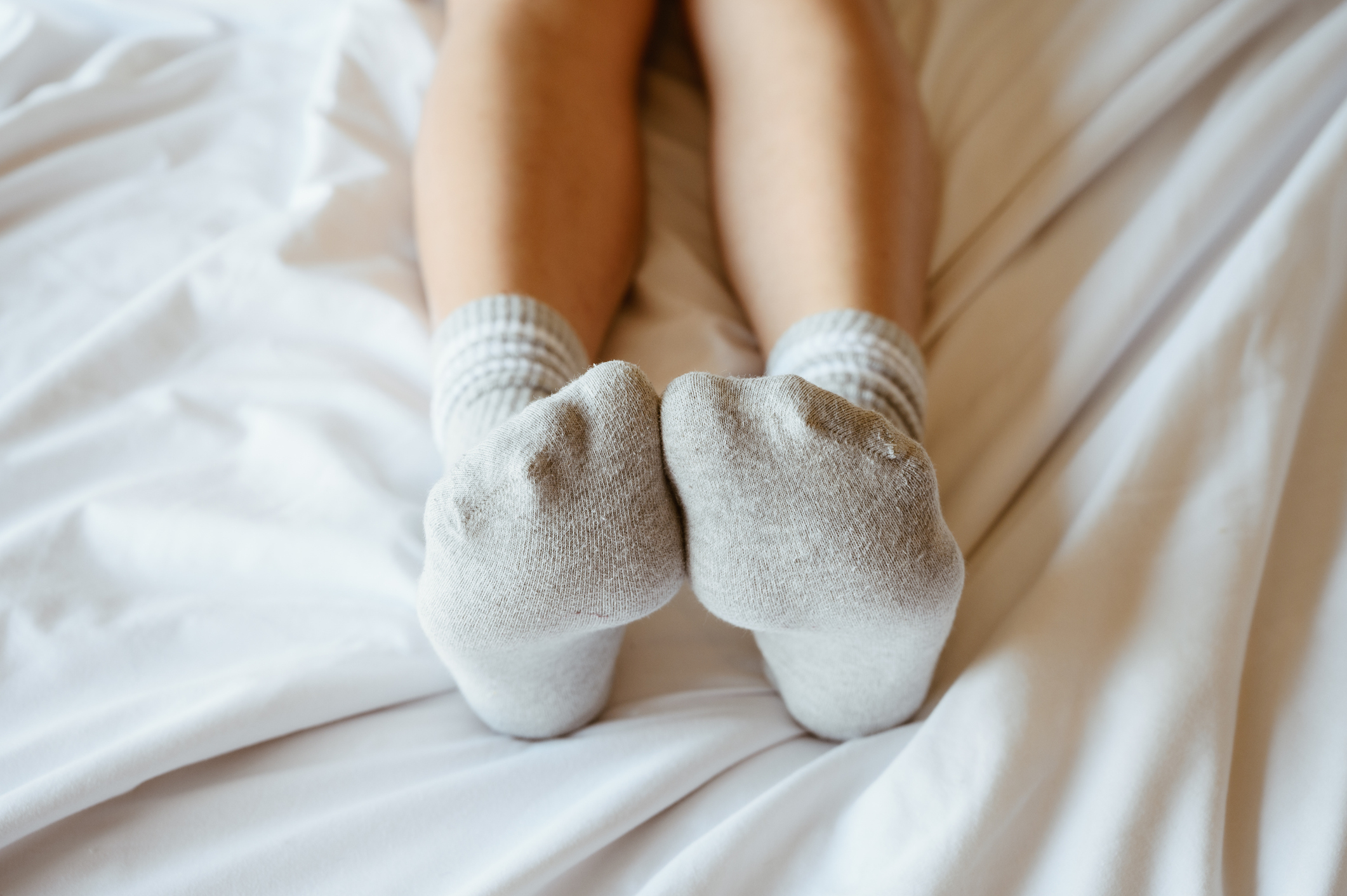 Person lying on a bed with their feet crossed, wearing plain socks, promoting relaxation