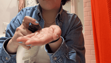 Person in denim jacket using a pump bottle to dispense lotion into their hand
