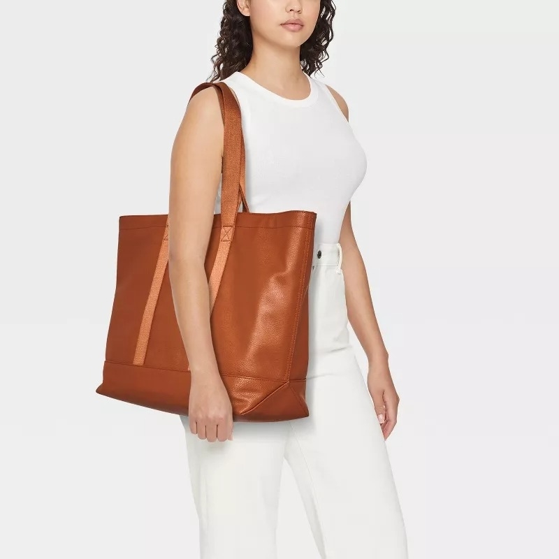 A model carrying a large brown tote bag on her shoulder