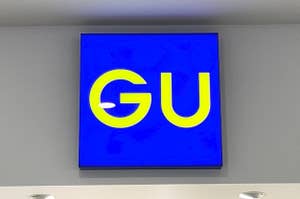 Sign with "GU" logo mounted on a wall, above what appears to be a store entrance