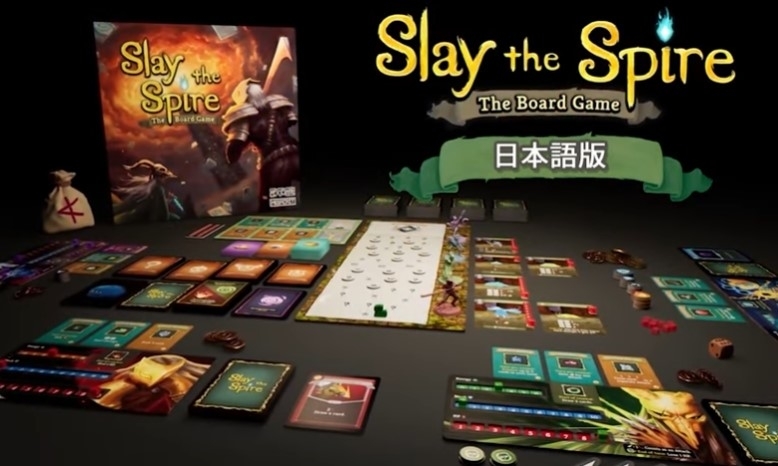 ボードゲーム「Slay the Spire」のプレイエリアが展開され、カードやコマが配置されている様子。発売予告のテキストあり。