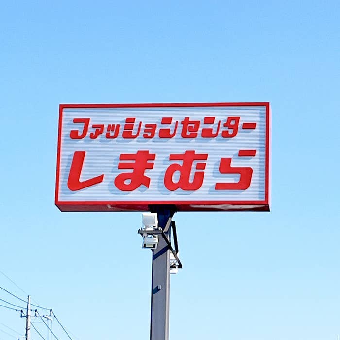 Sign in Japanese on a pole under a clear sky, likely a store name or advertisement