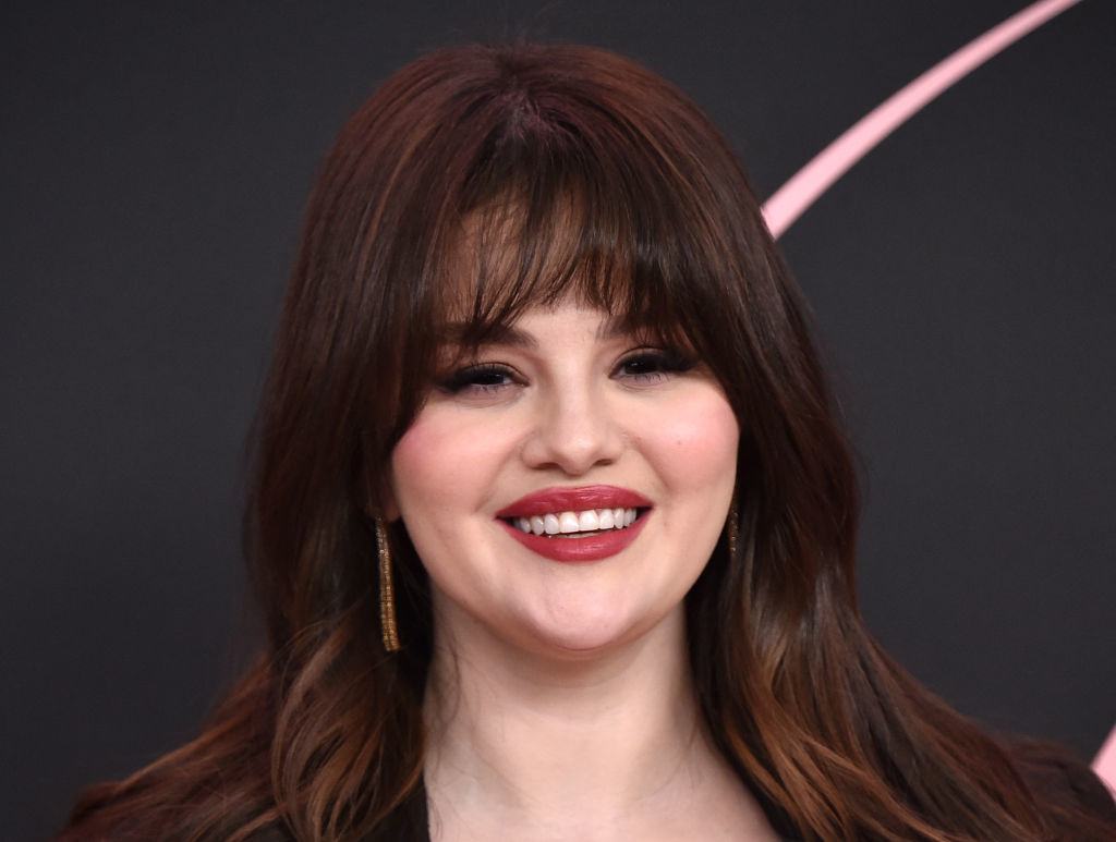 Selena Gomez smiling at an event, wearing dangling earrings and a v-neck outfit