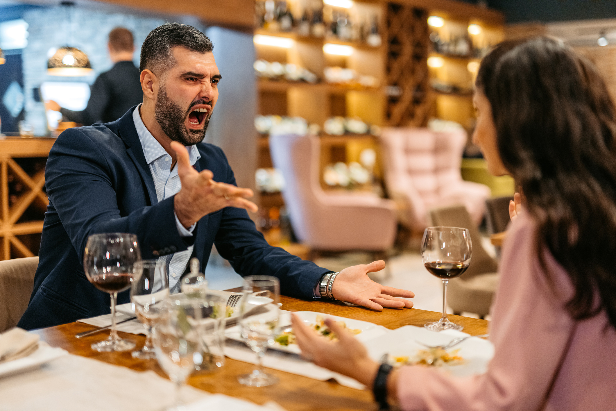 Man gesturing animatedly during a discussion with a woman at a restaurant table