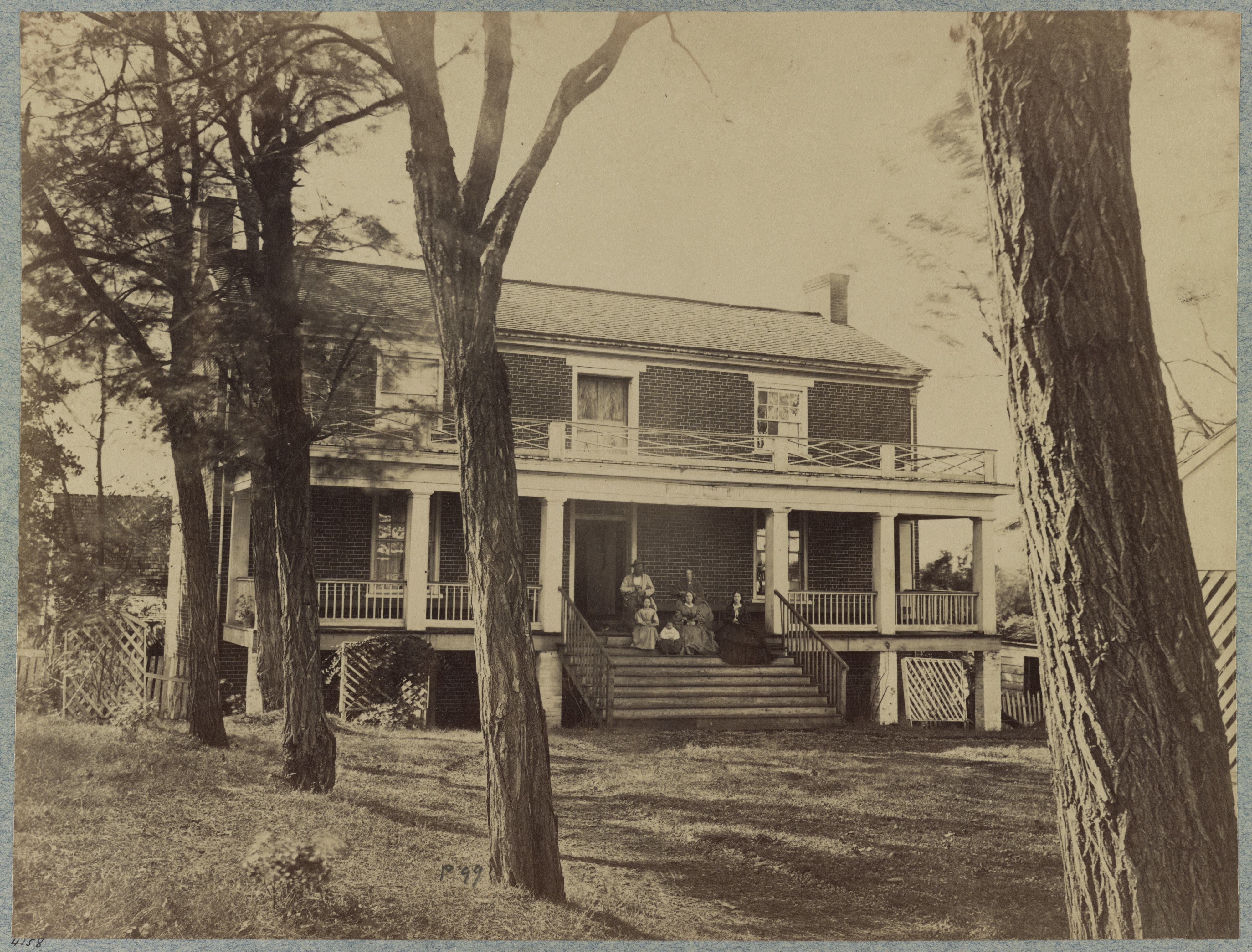 Historic photo of a two-story house with a porch and people sitting outside
