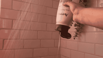 Hand squeezing shampoo from a bottle into a shower with running water