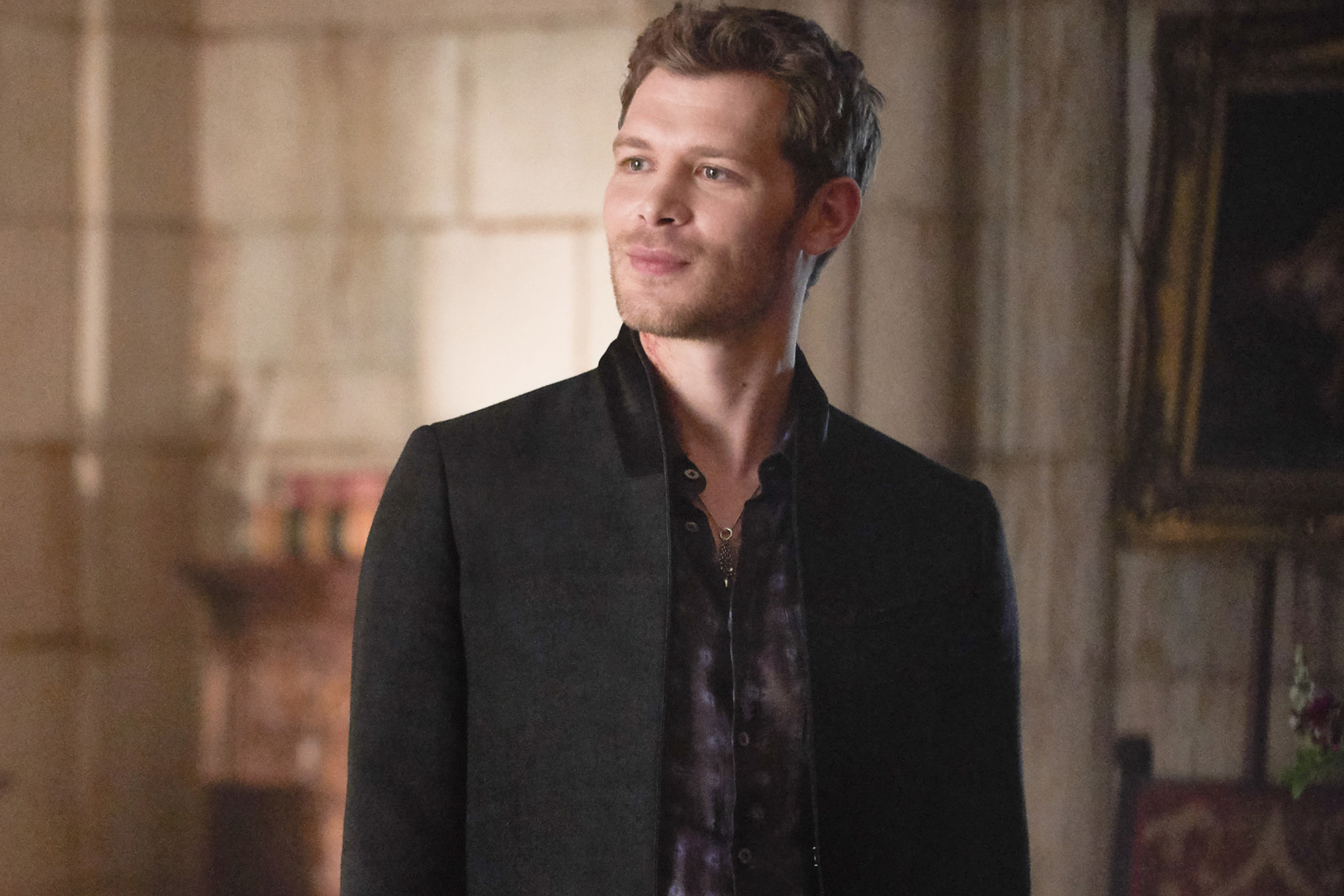 Joseph Morgan in a black blazer over a patterned shirt, smiling on the TV show set