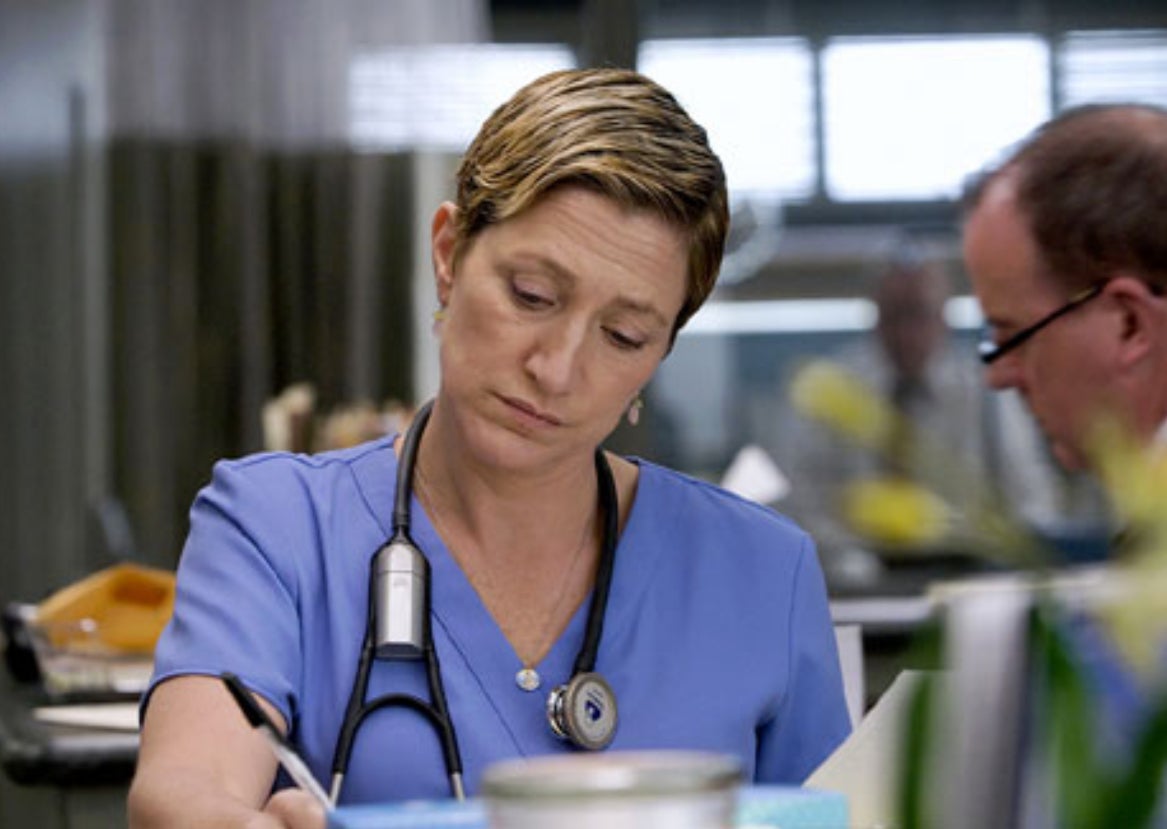 Edie Falco as Nurse Jackie in scrubs focused on paperwork, medical setting