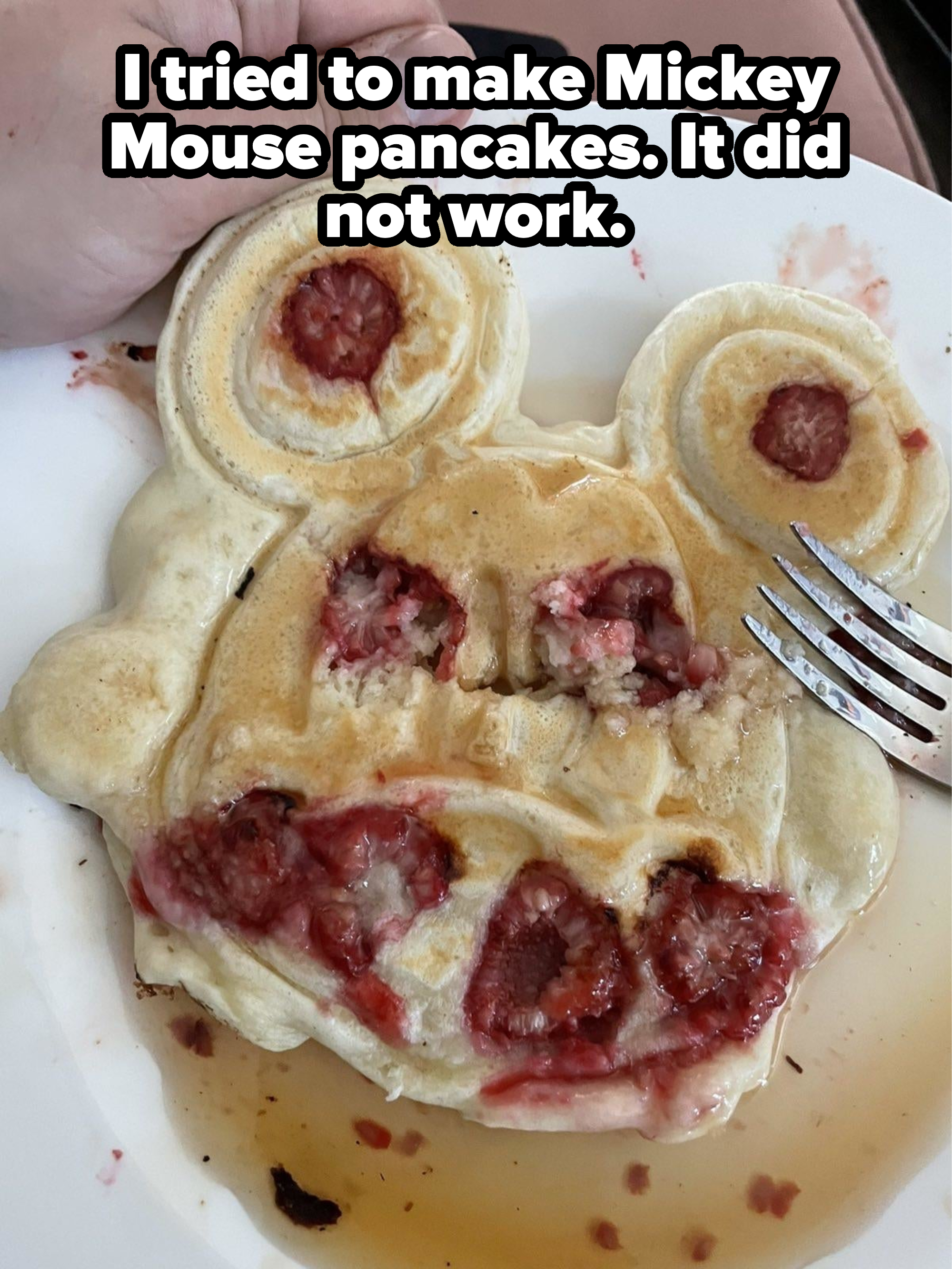 Pancake with smiley face design and embedded strawberries, partially eaten, on a plate with a fork