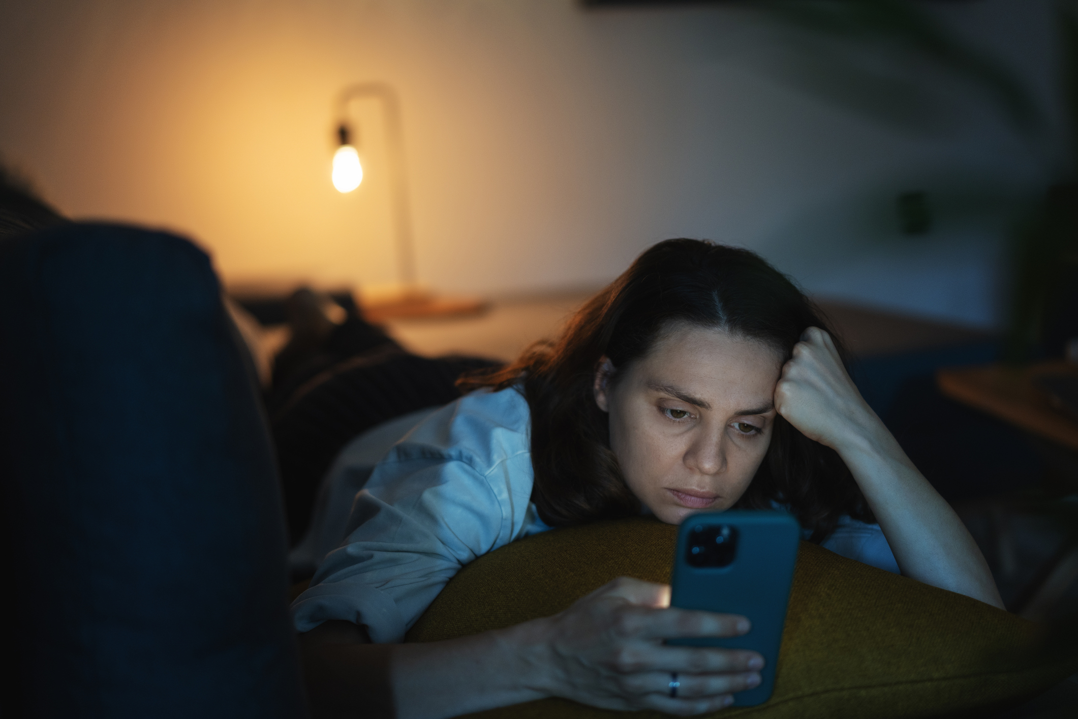 Woman lying on a couch looking at her smartphone with a concerned expression