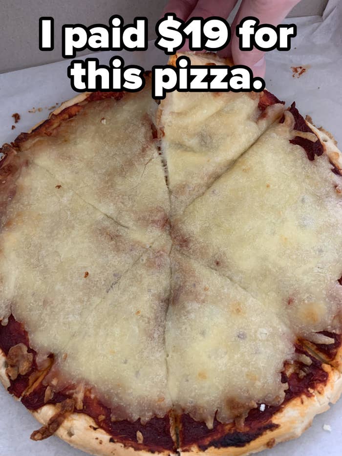A hand is lifting a slice from a cheese pizza inside a box, with one slice already removed