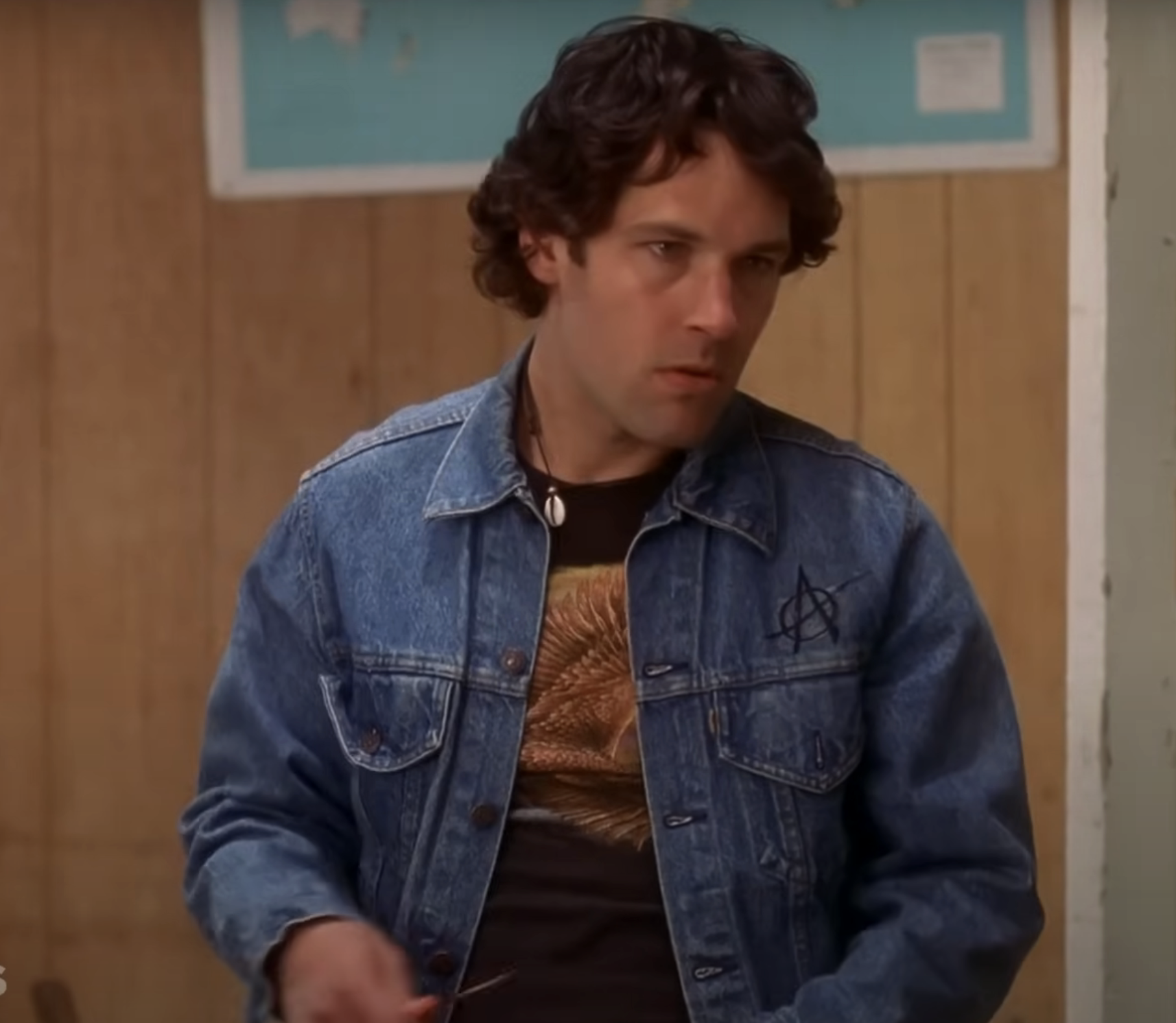 Andy in denim jacket over sweater, standing indoors, concerned expression