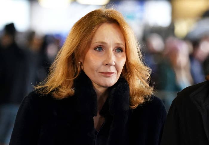 JK Rowling with shoulder-length hair in a coat, fur collar, looking away, slightly smiling