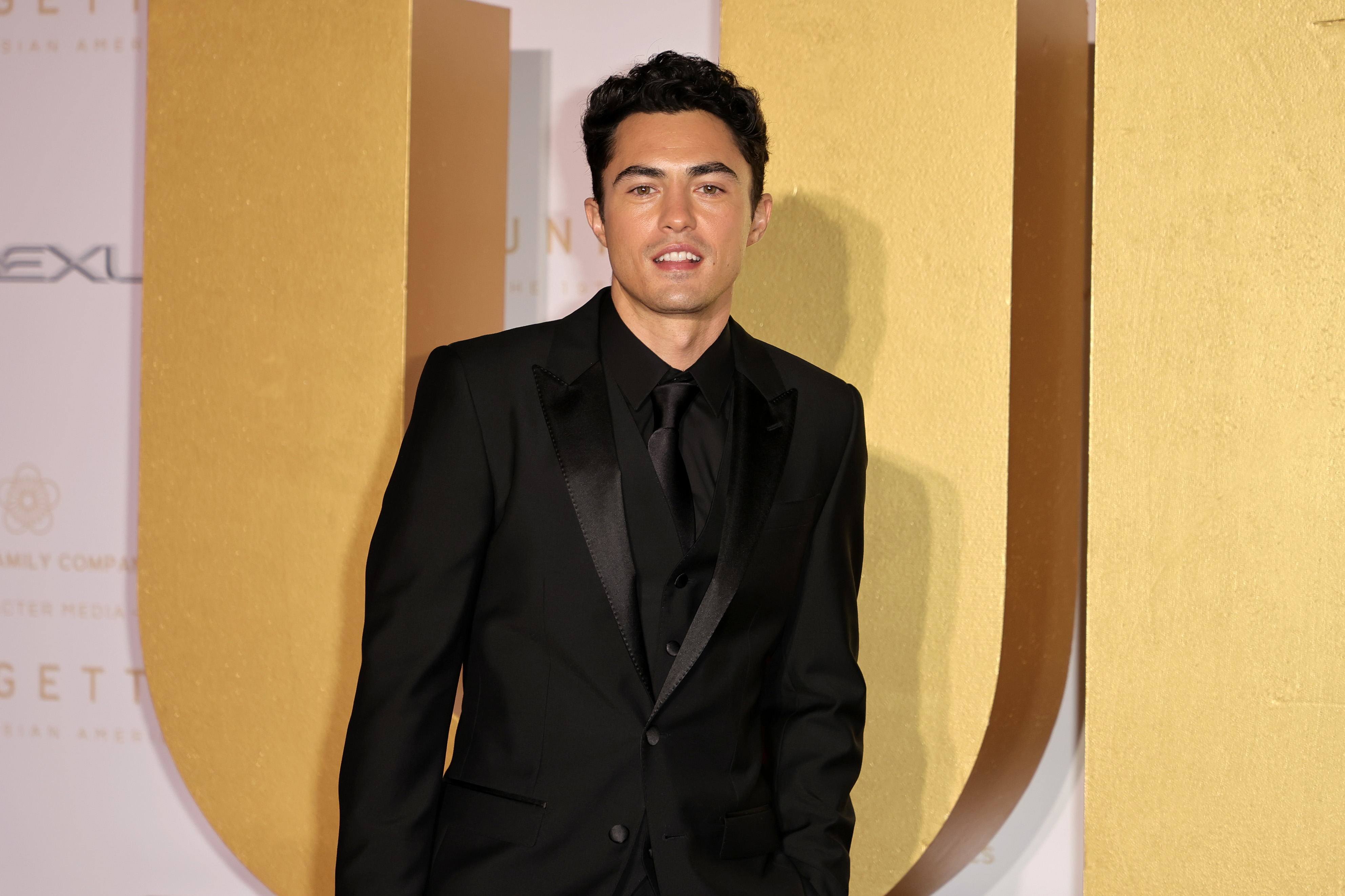 Darren in suit posing in front of a golden backdrop