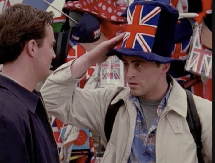 Two men in a crowded area, one adjusting a novelty hat on the other&#x27;s head