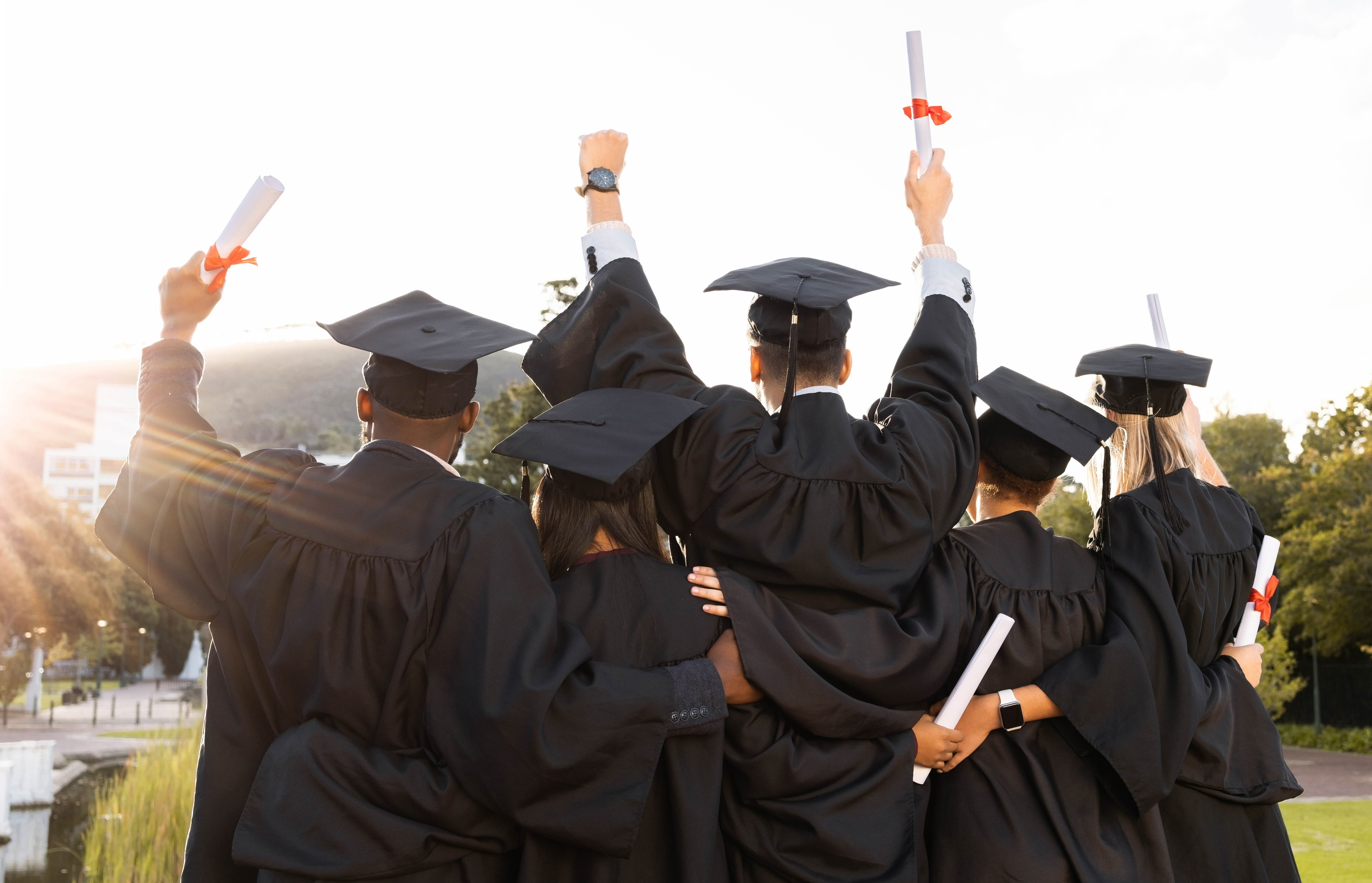 Graduates in caps and gowns, raising diplomas, embracing, celebrating achievement