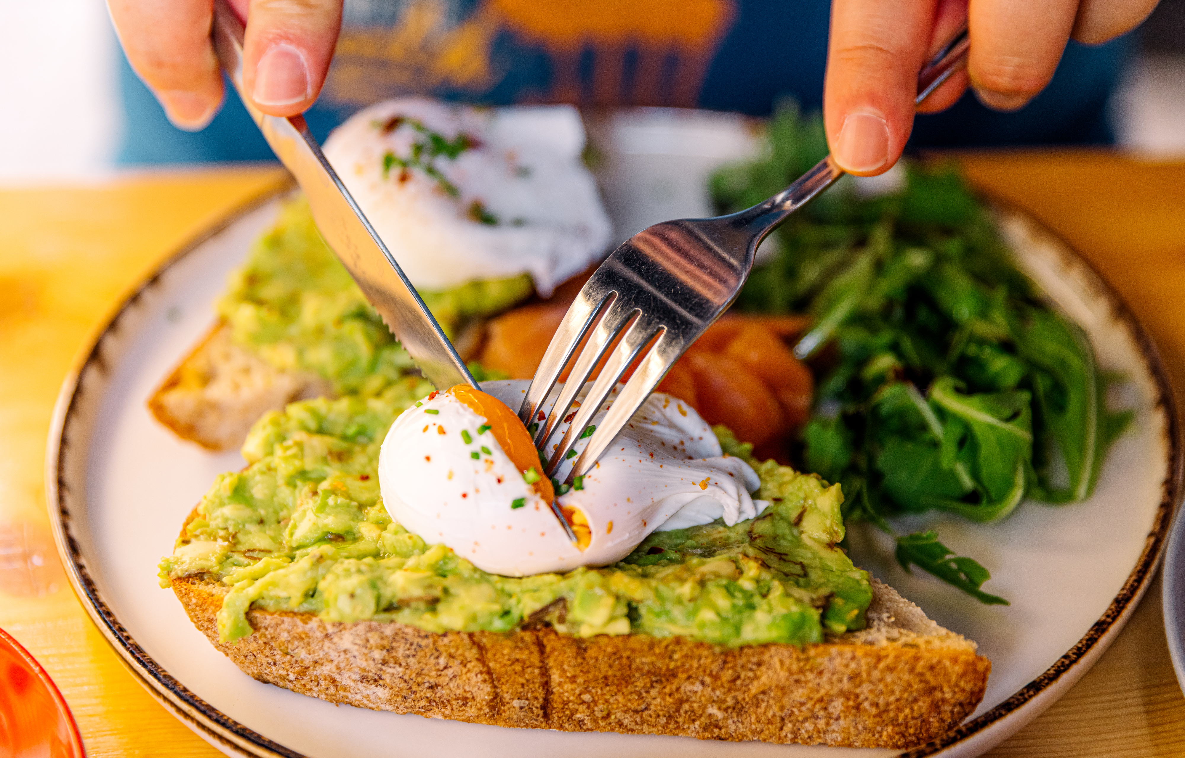 Person cutting into a poached egg on avocado toast with a side salad