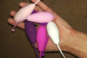 A hand holds a set of kegel exercise devices in varying colors and sizes