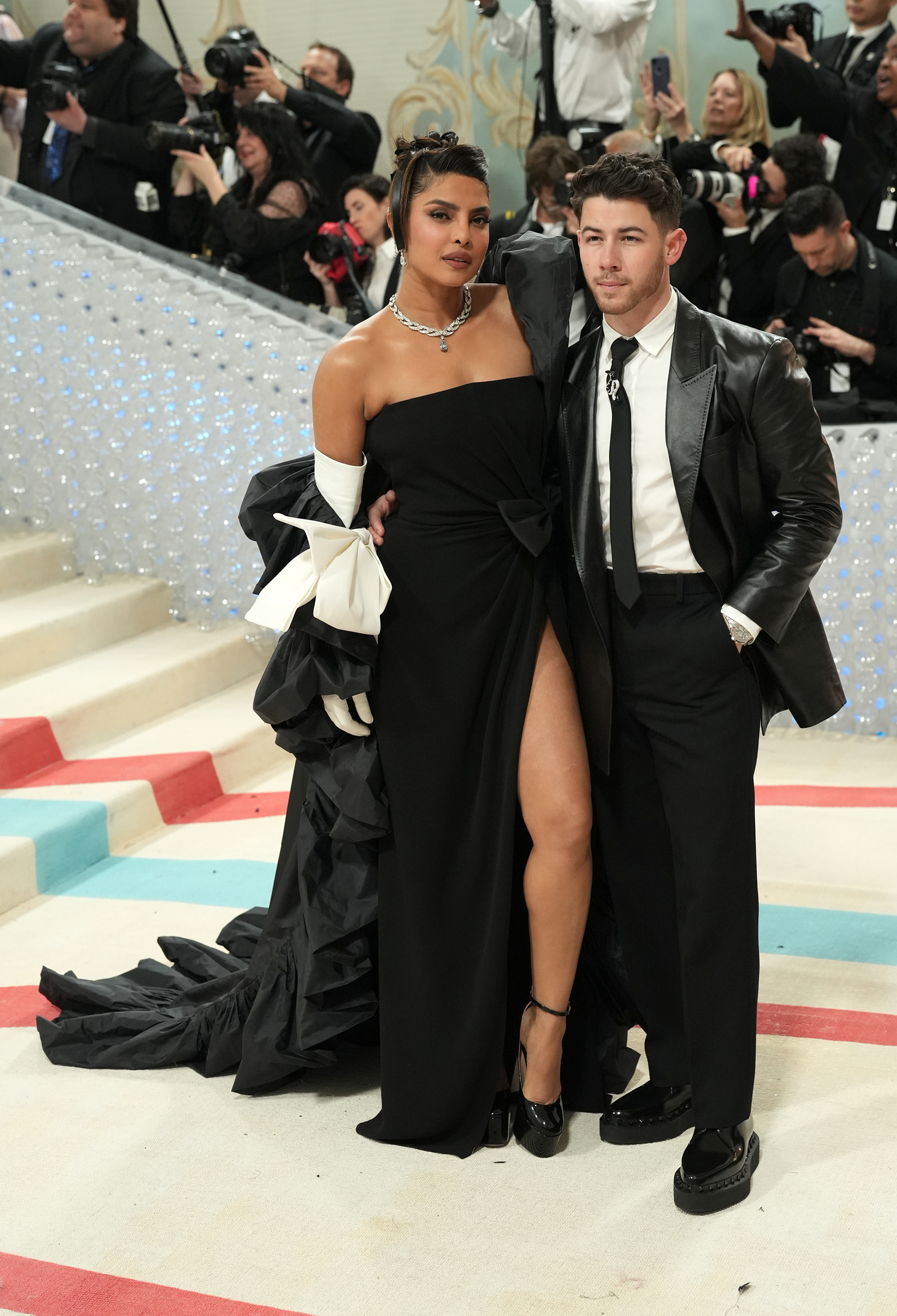 Priyanka Chopra in a black gown with a high slit and Nick Jonas in a black suit on the Met Gala stairs