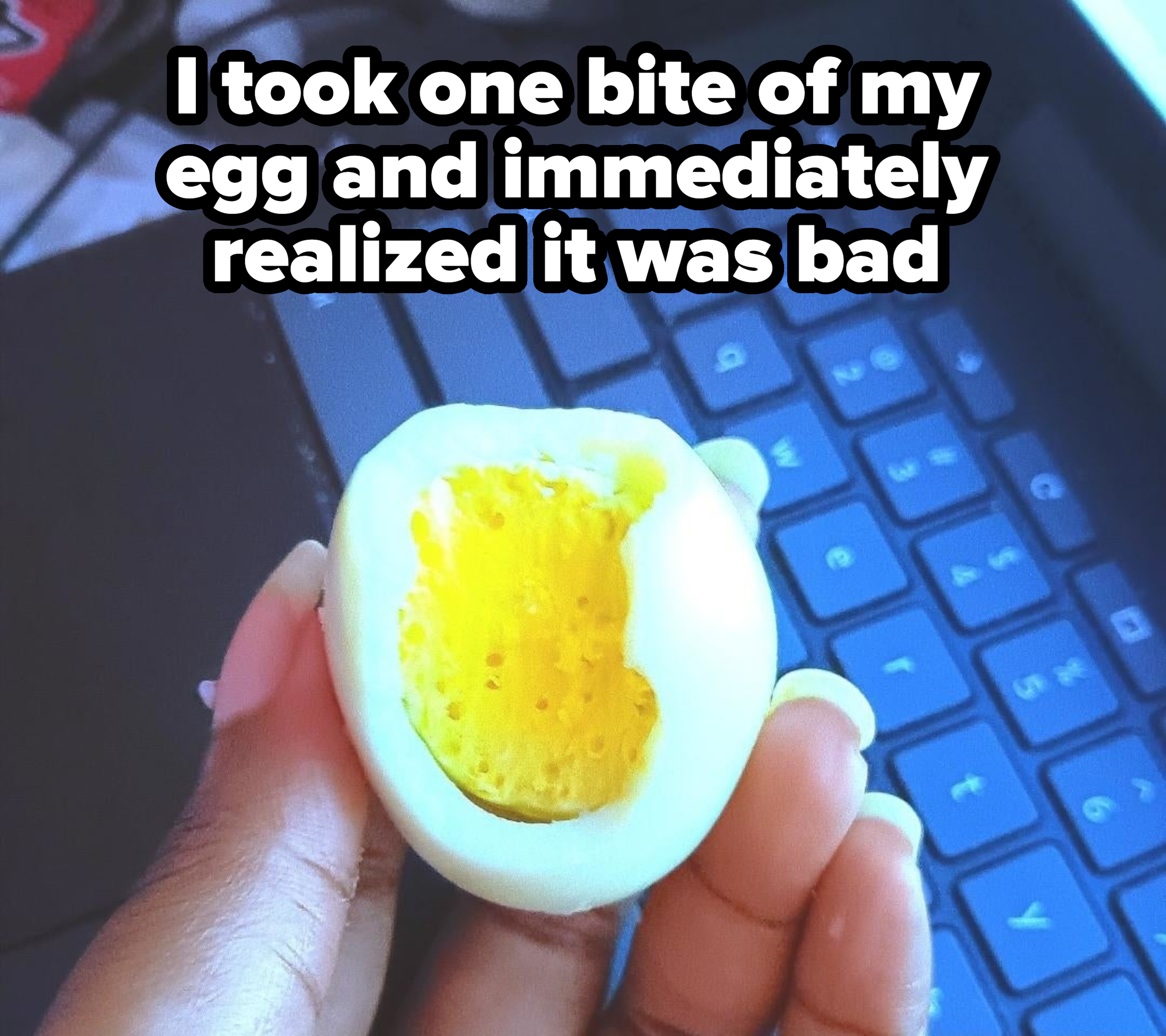 Person holding a half-eaten boiled egg over a laptop keyboard