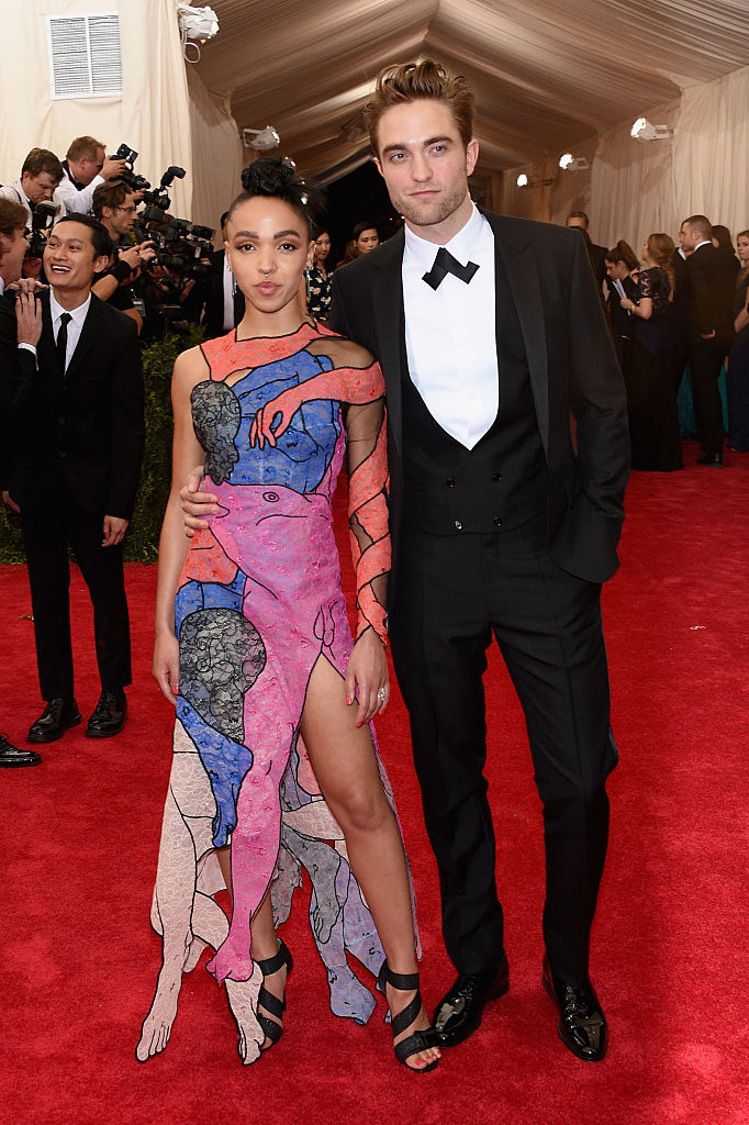 Two celebs standing together; one in a mosaic-inspired cutout dress and the other in a classic tuxedo