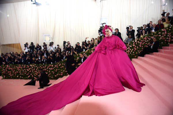 Lady Gaga in voluminous pink gown with bow accents at a Met Gala event, posing on stairs