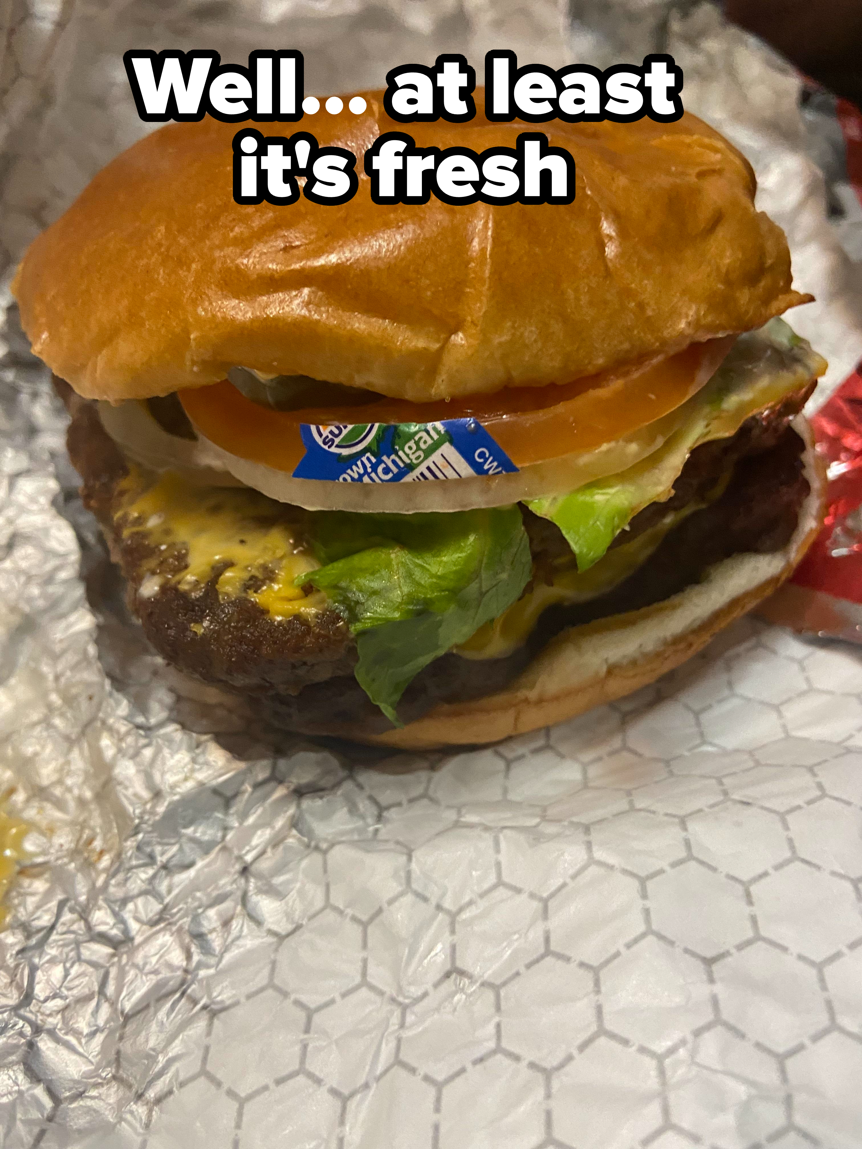Cheeseburger with lettuce, tomato, and a sticker accidentally left on the cheese
