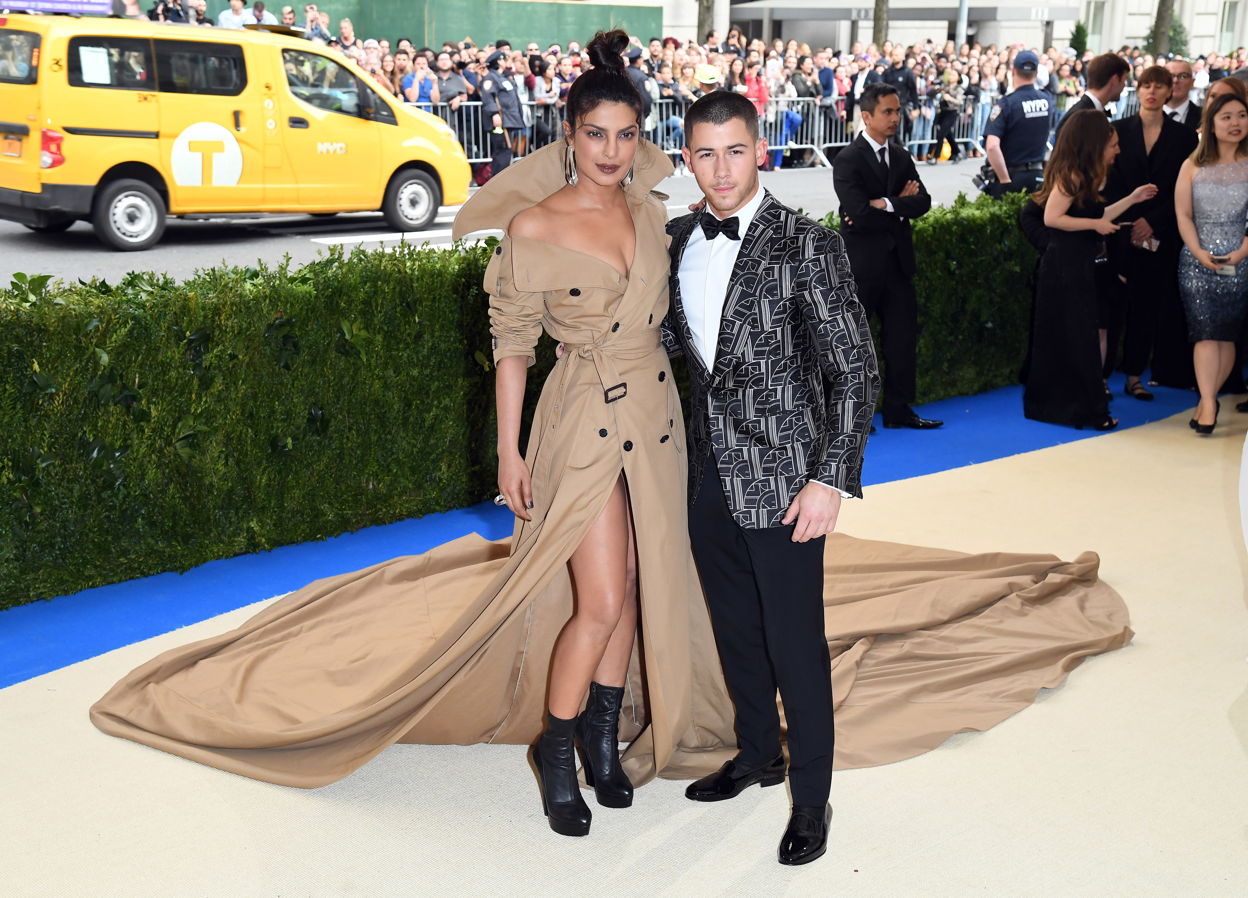 Priyanka Chopra in a trench coat-inspired dress with a long train and Nick Jonas in a patterned tuxedo on the red carpet
