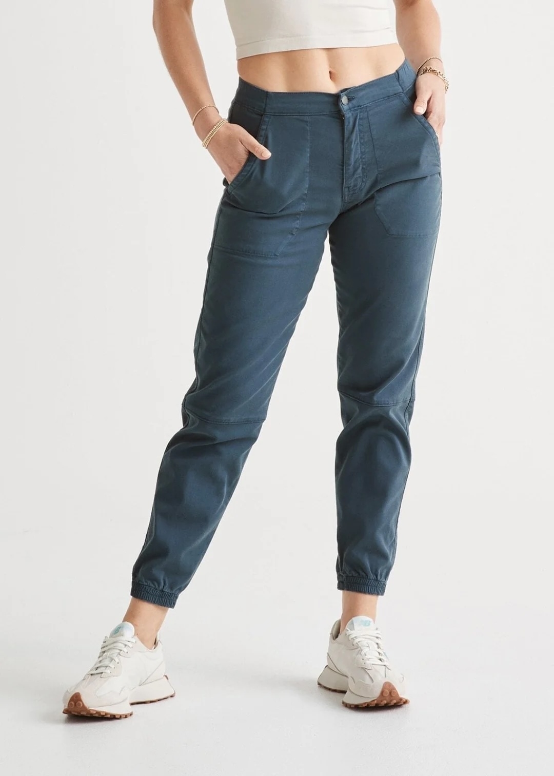 A model wearing  blue mid-rise casual pants with pockets paired with sneakers, showing from the waist down